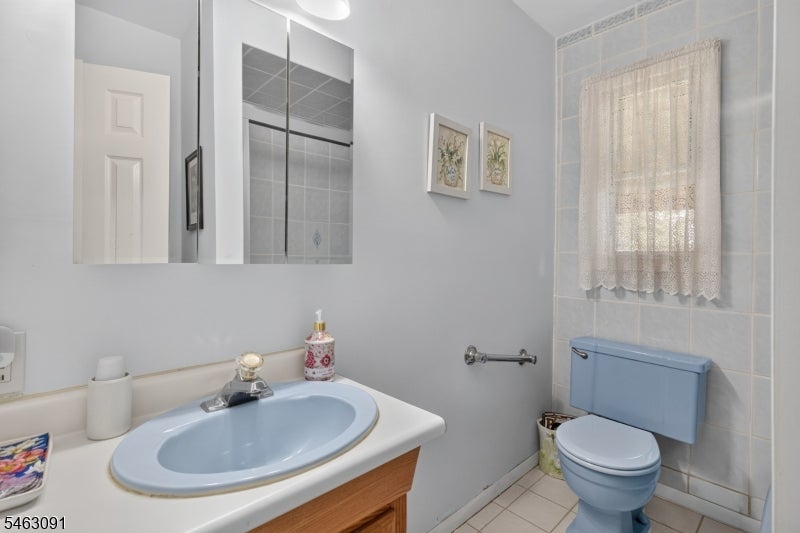 Bathroom with a light blue sink and toilet, wood vanity, and lace-curtained window.
