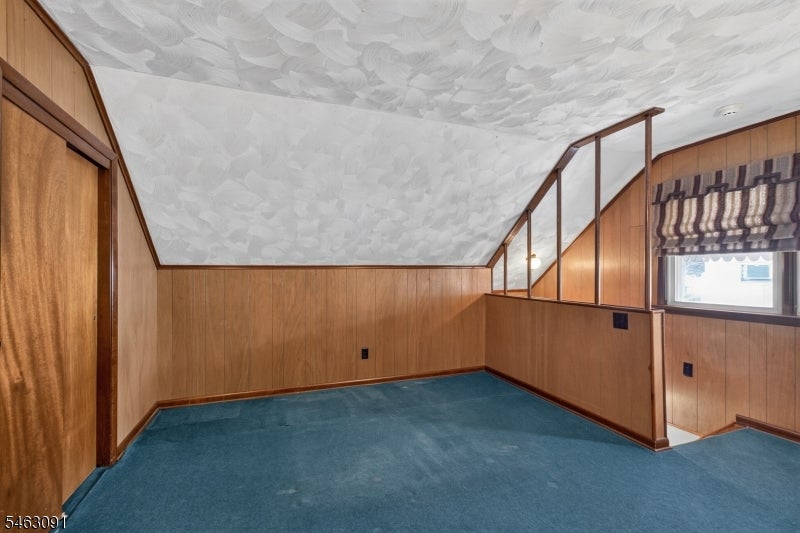 Vacant carpeted room with wood-paneled walls, a sloped ceiling, and a railing beside the window.