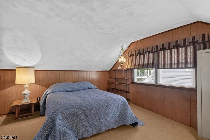 Bedroom with a blue quilted bed, wood-paneled walls, and a sloped ceiling.