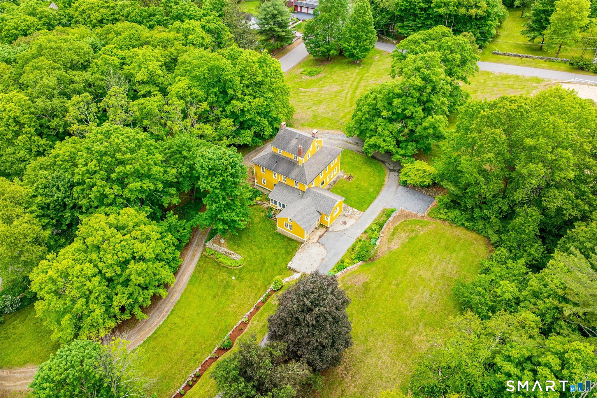 Aerial view of a yellow house amid mature trees, open lawns, and a curving driveway.