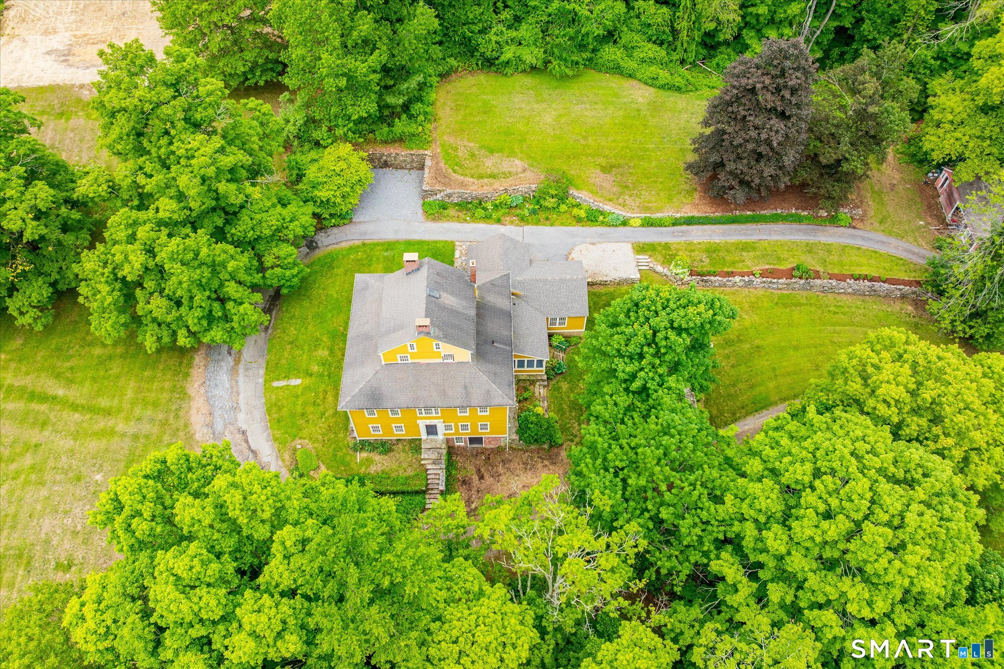 Aerial view of a yellow house amid mature trees, lawns, and a curving driveway.