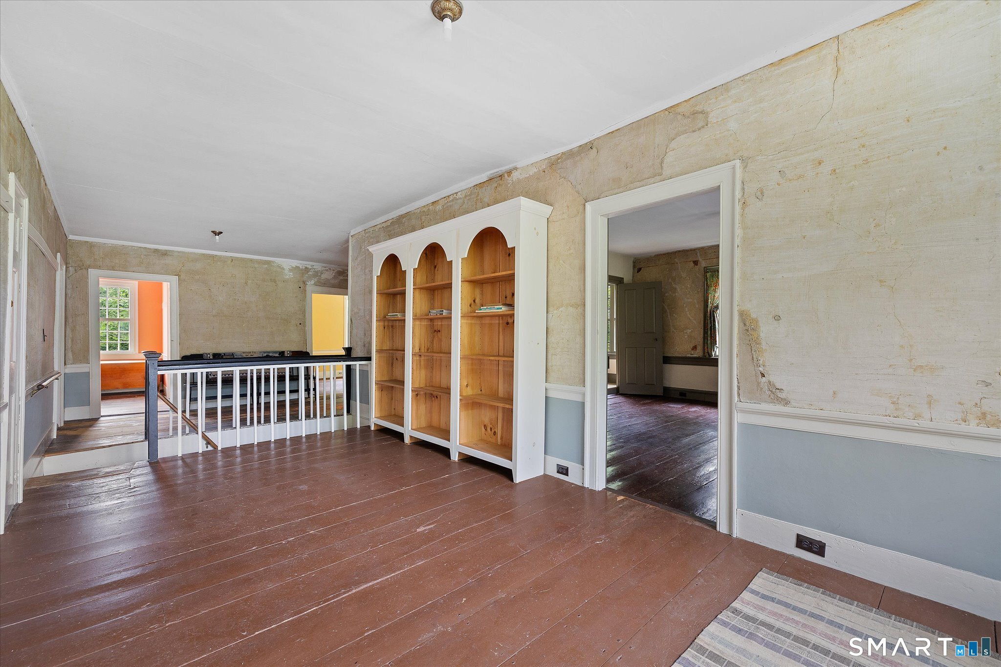 Landing with built-in arched bookcase, worn plaster walls, and dark wood plank flooring.