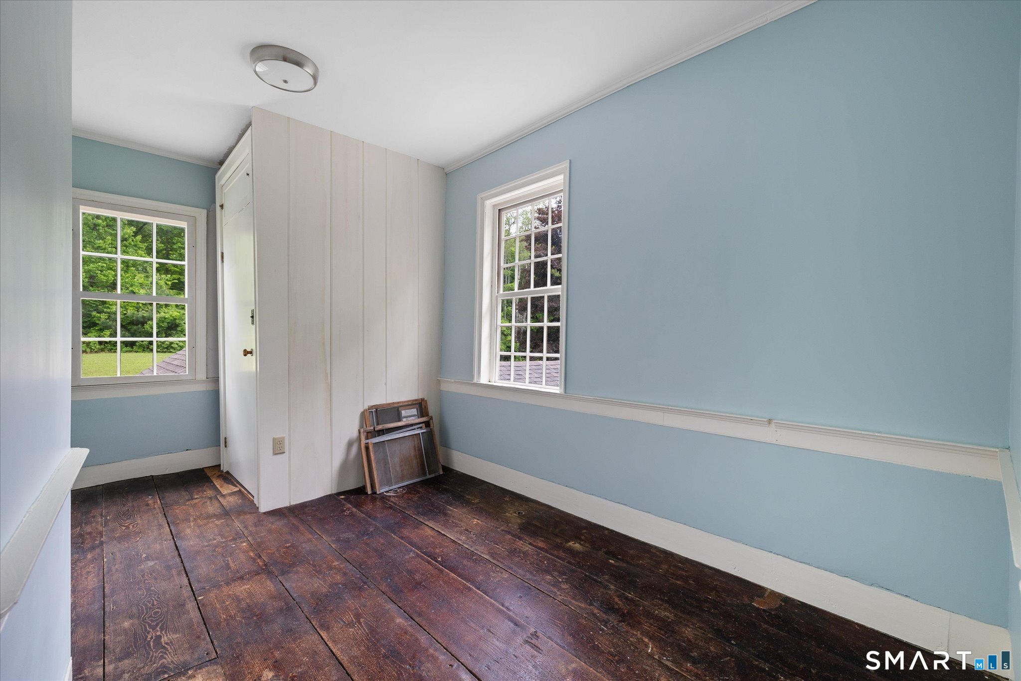 Unfurnished blue room with a built-in closet, two windows, and dark wide-plank floors.