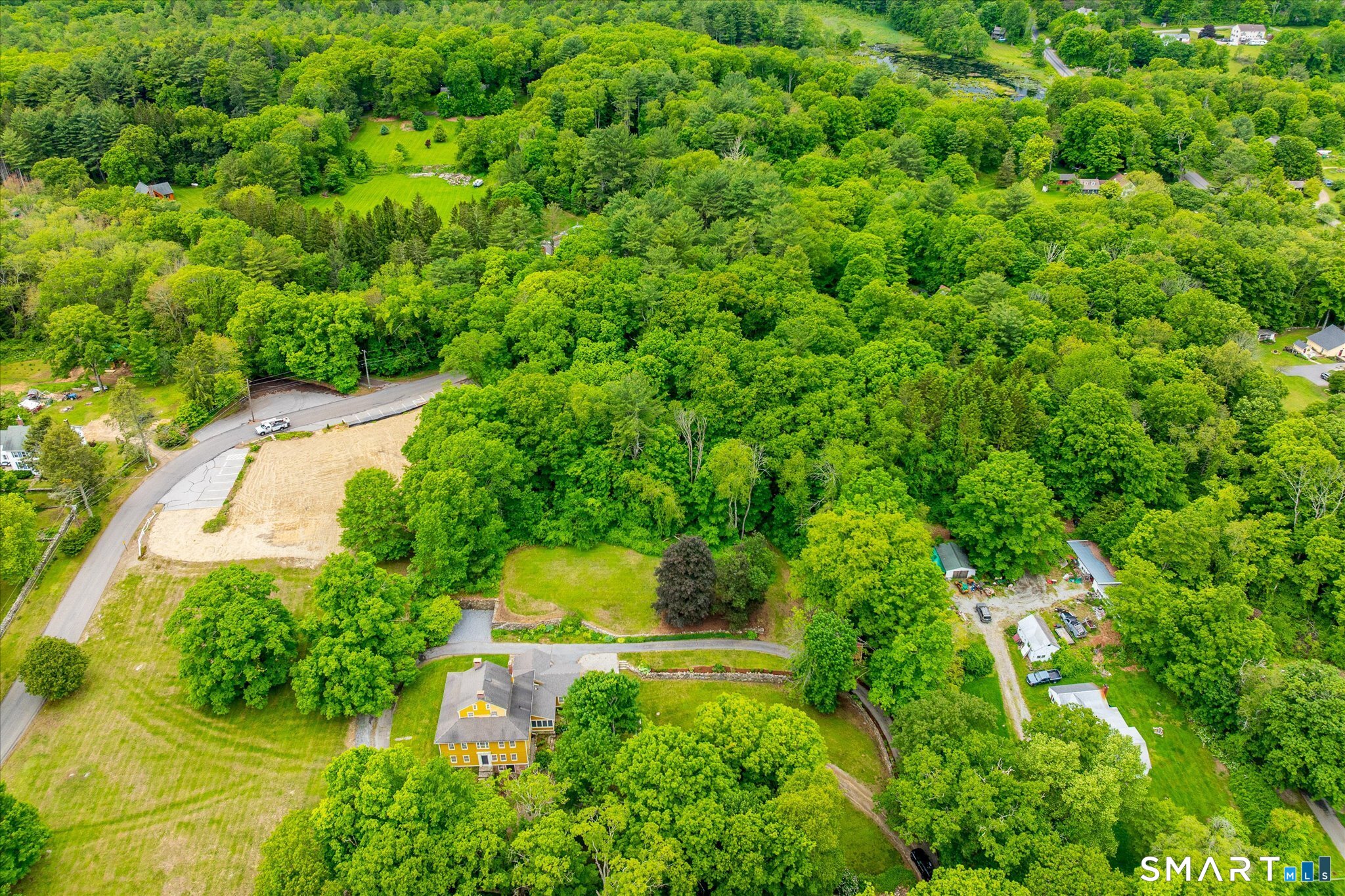 Aerial view of a yellow house surrounded by mature trees and open lawn.