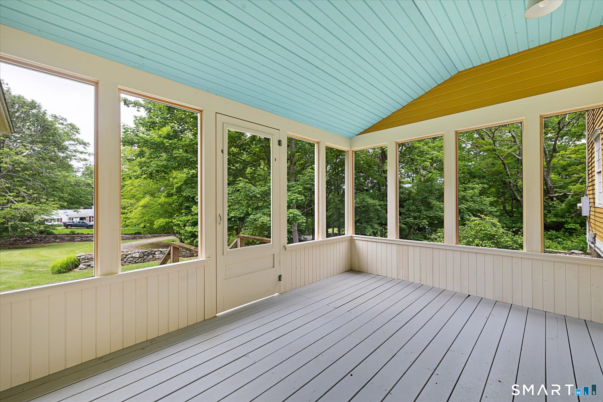 Enclosed porch with a blue plank ceiling and large windows overlooking trees and lawn.