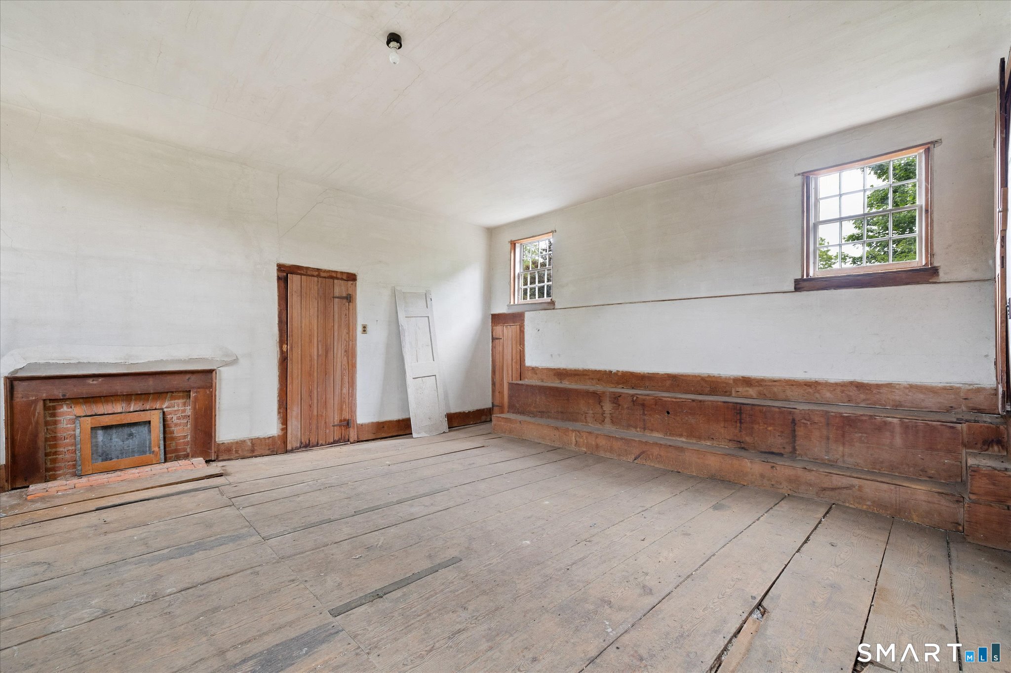 Vacant room with a brick fireplace, wide plank floors, and a long built-in wooden bench.