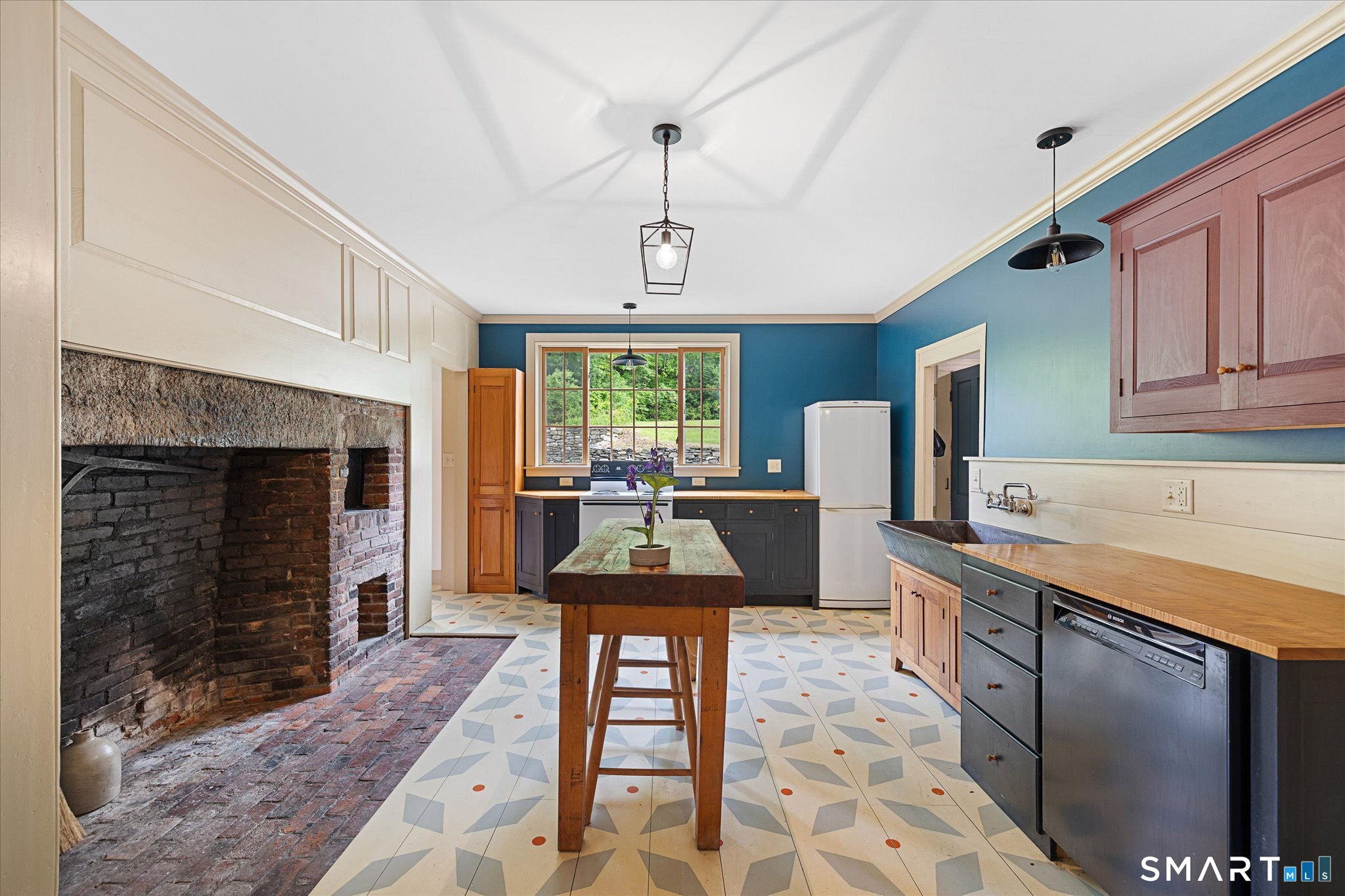 Kitchen with a large brick fireplace, blue walls, patterned tile floors, and a central wooden island.