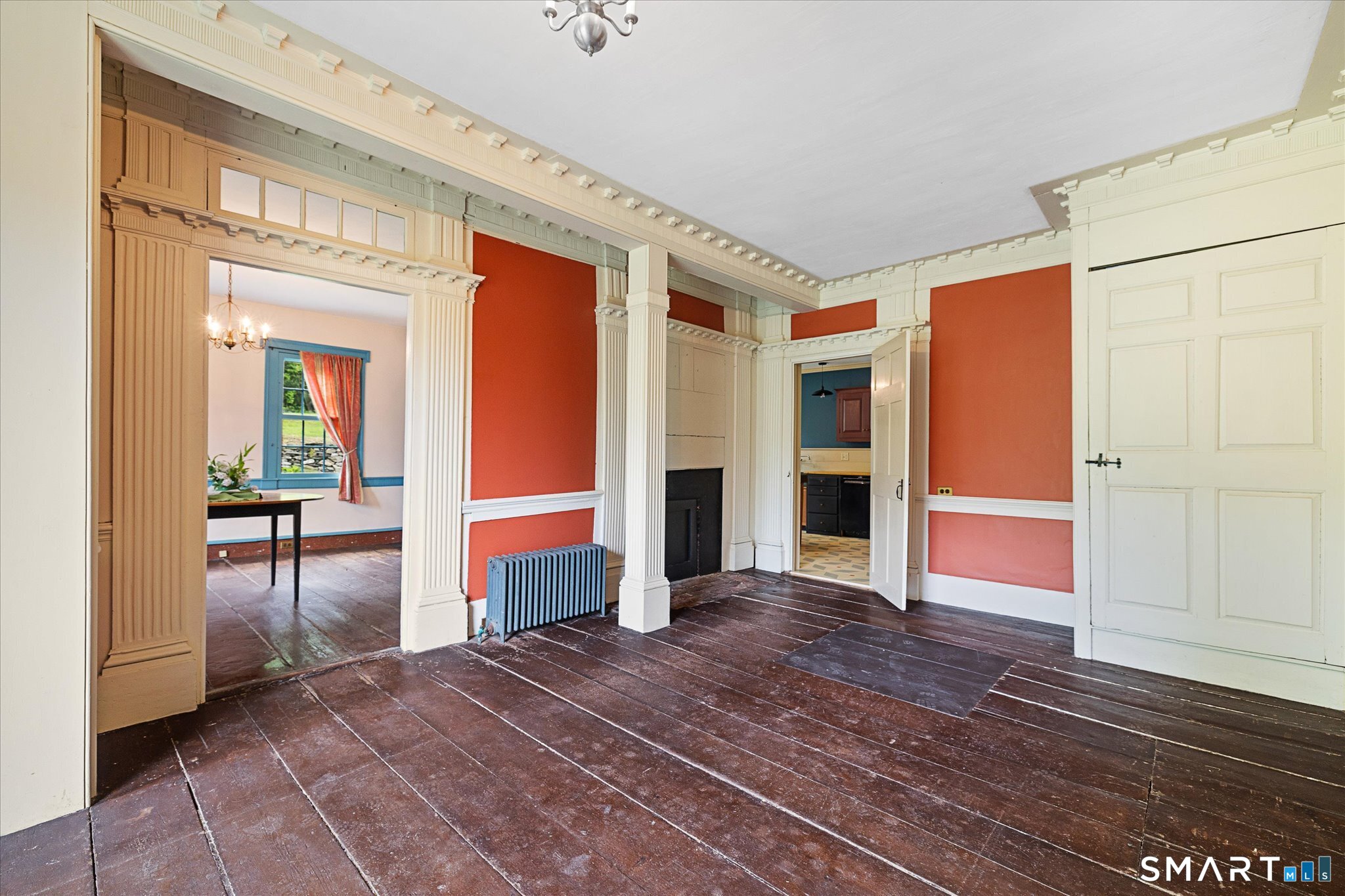 Historic home interior with red walls, ornate cream columns, dark plank floors, and a blue radiator.