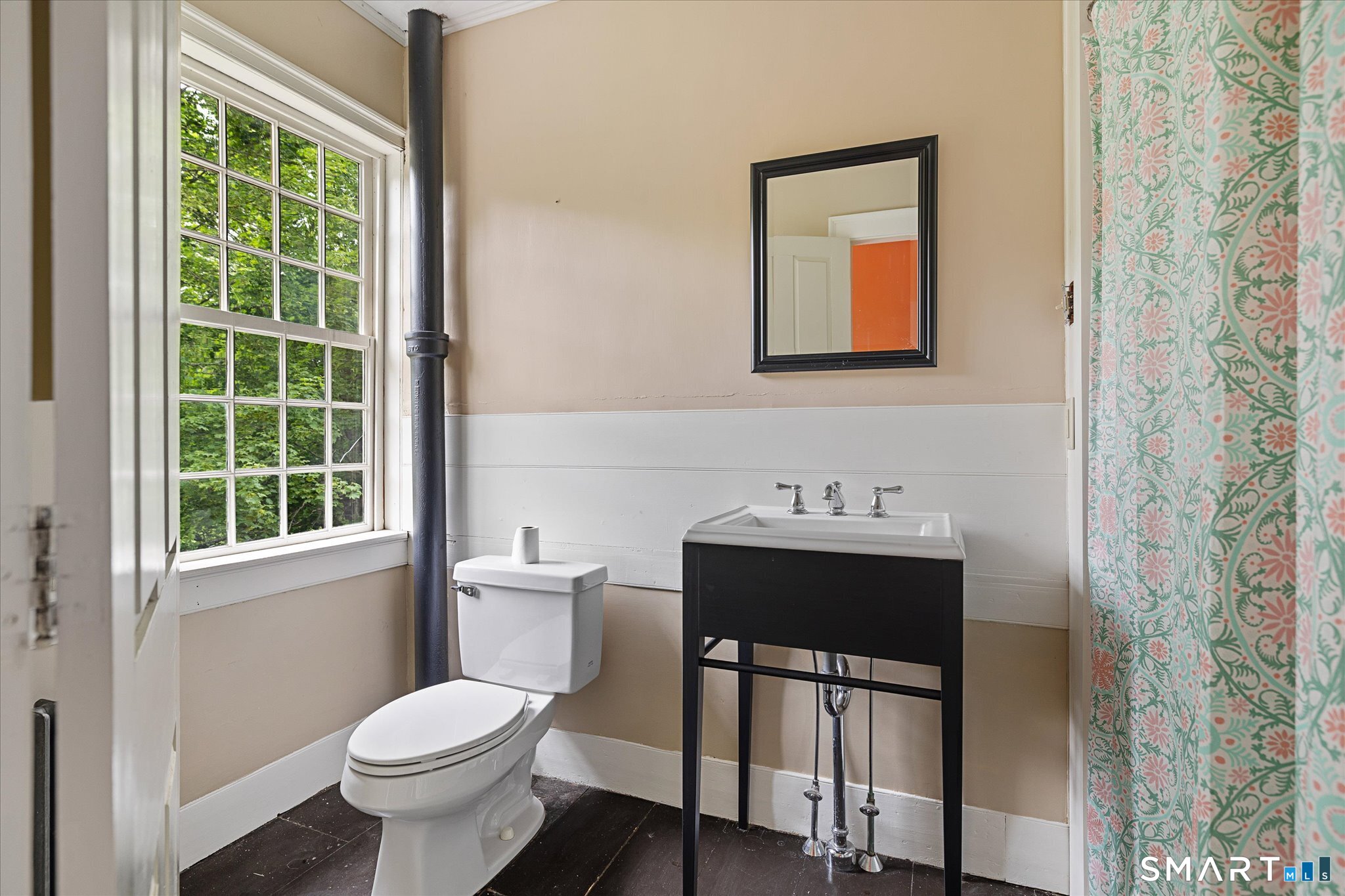 Bathroom with a large tree-facing window, black vanity, exposed pipe, and floral shower curtain.