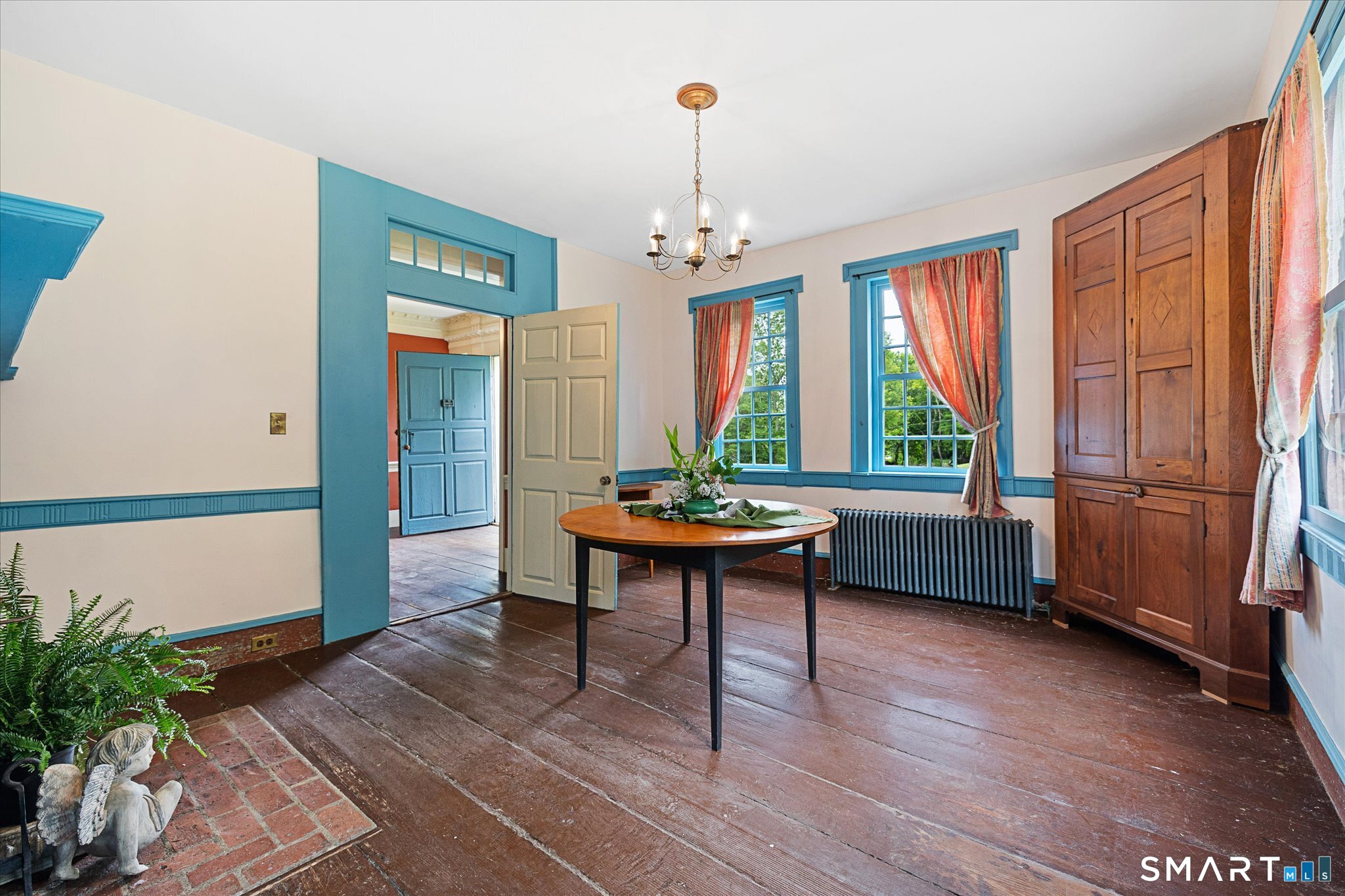 Dining room with blue trim, curtained windows, wide-plank floors, and a built-in wooden cupboard.