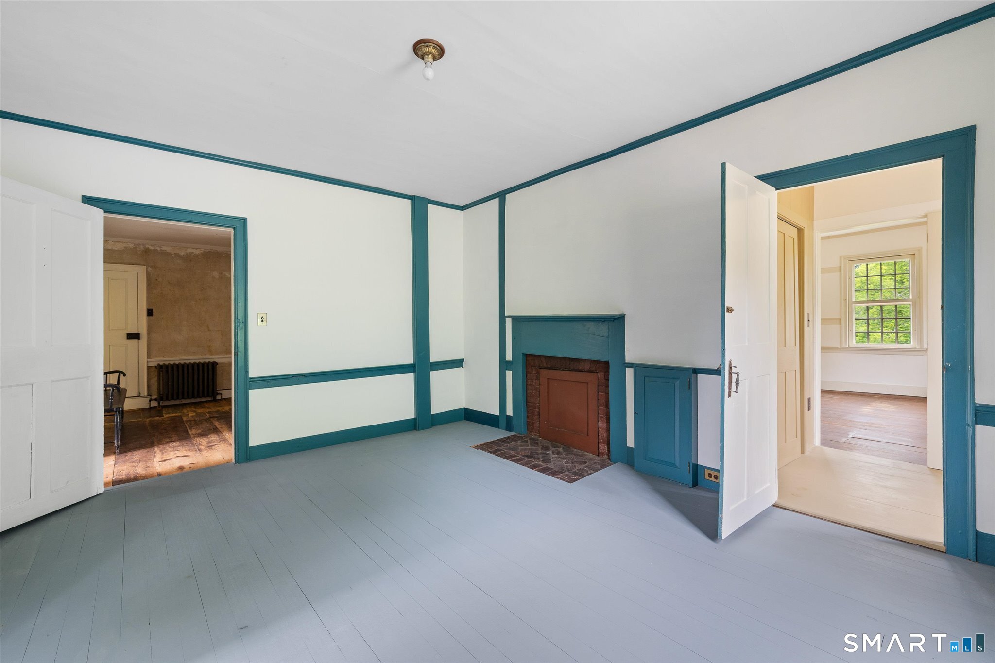 Vacant room with teal-trimmed walls, plank flooring, a brick fireplace, and open doorways to adjoining rooms.