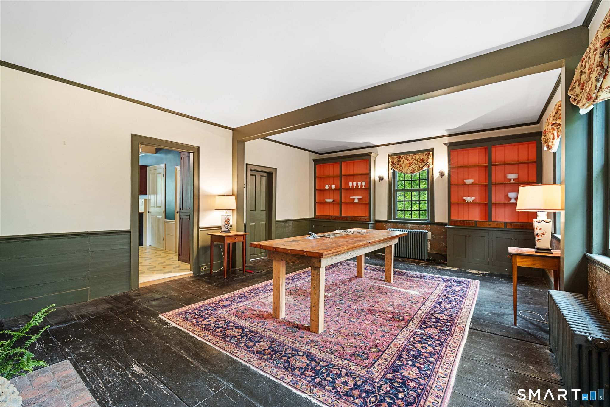 Furnished room with orange built-in shelves, a rustic wooden table, and a large patterned rug.