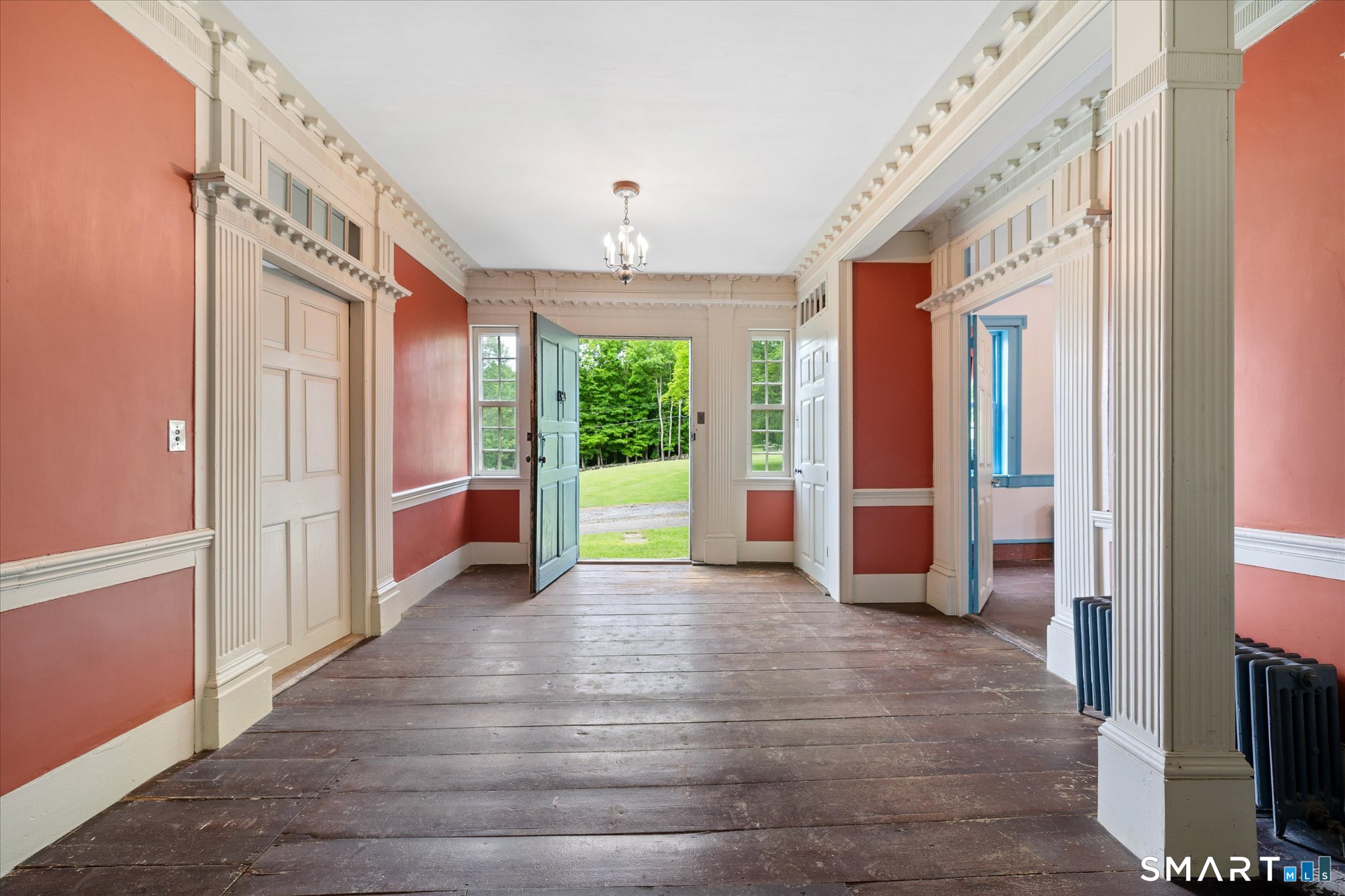 Entry hall with ornate cream trim, coral walls, wood floors, and an open blue-green front door.