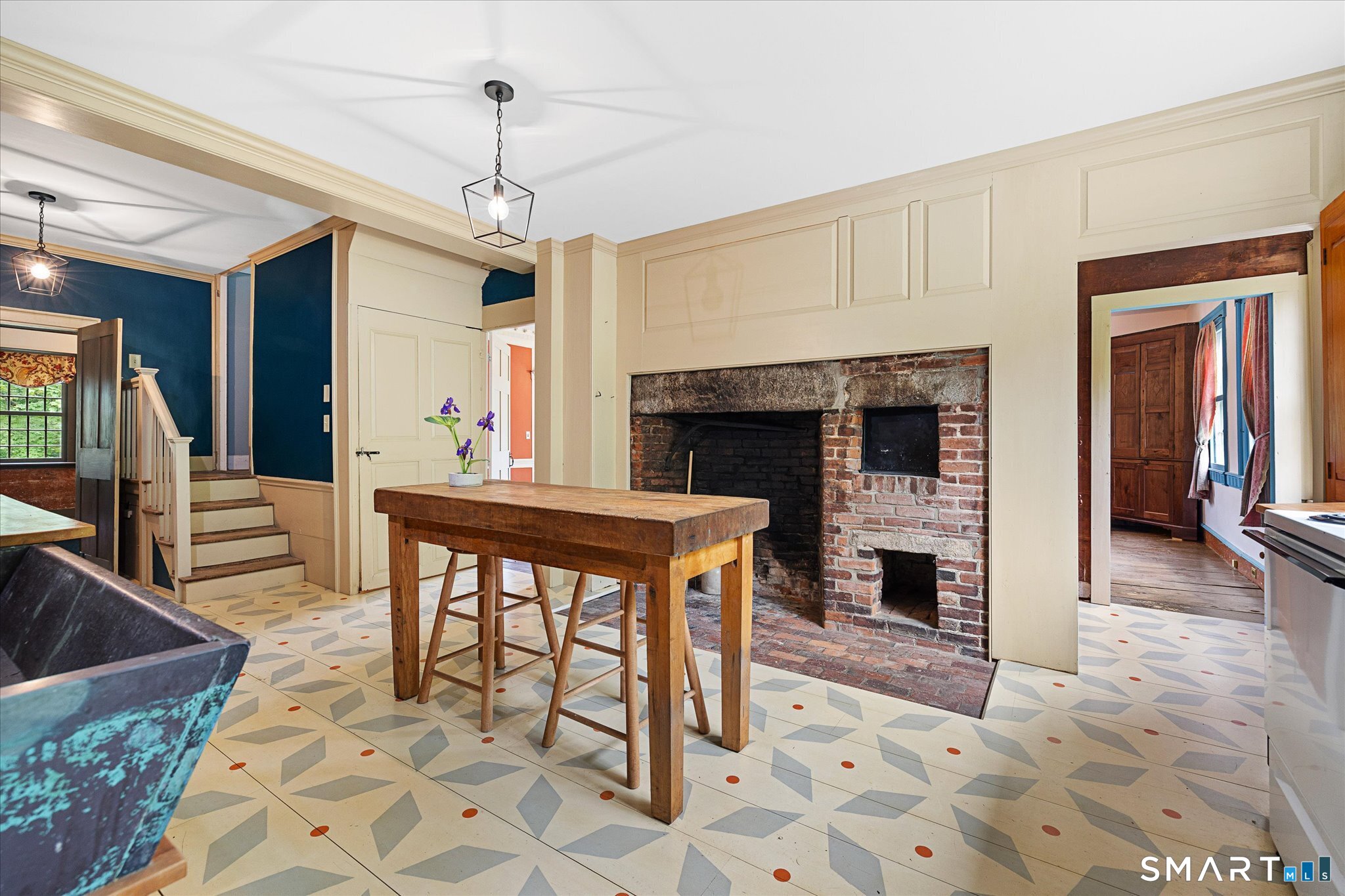 Kitchen with a brick fireplace, rustic worktable, and patterned tile floor.