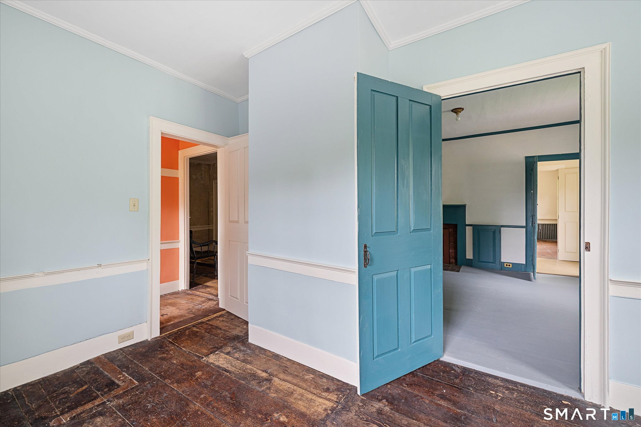 Interior hallway with worn wood floors and open teal doors leading to adjoining rooms.