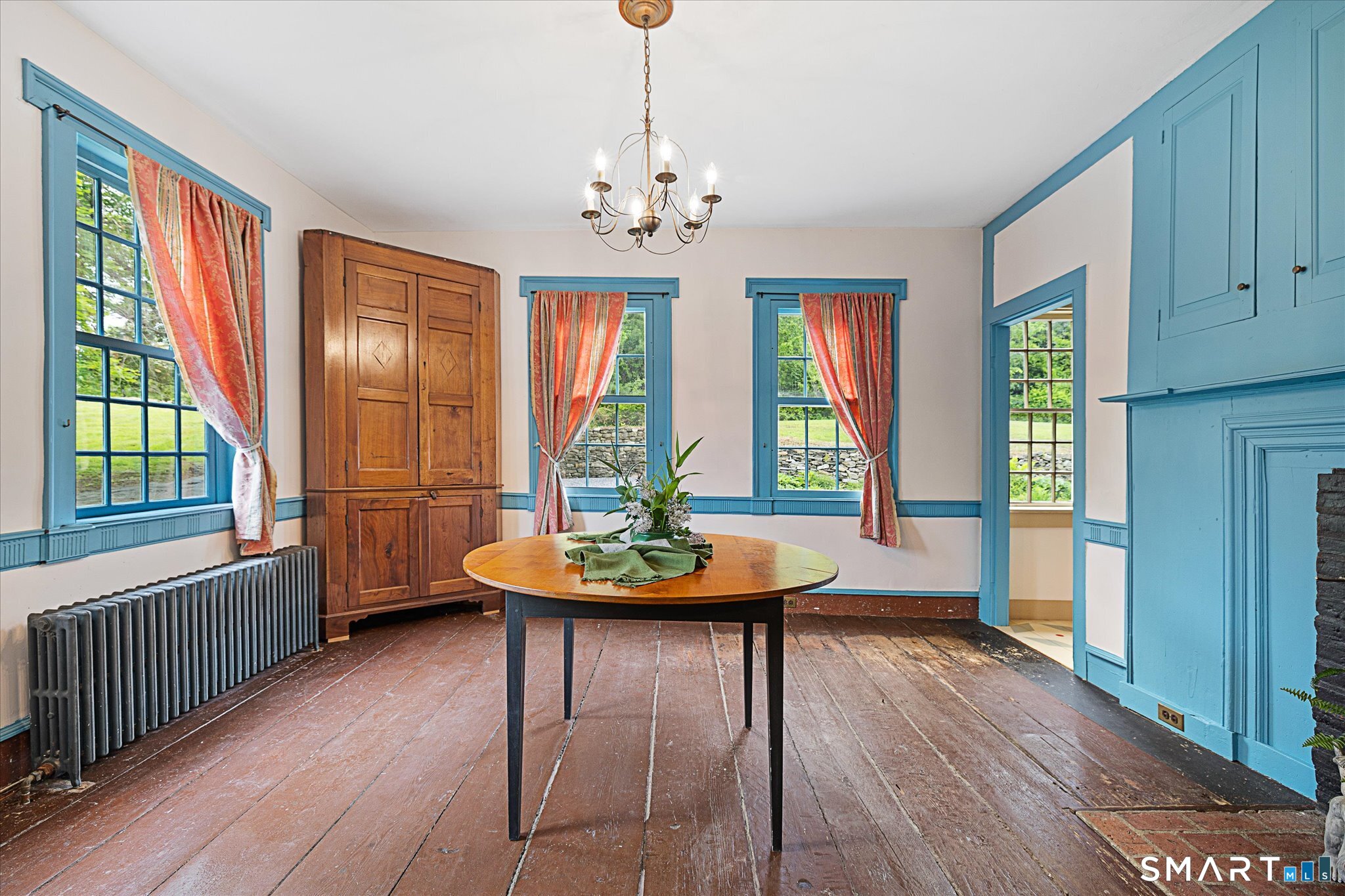 Dining room with blue trim, coral curtains, an antique cupboard, and a round wooden table.