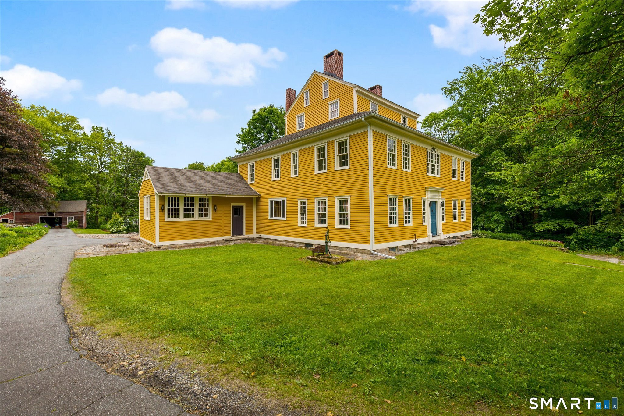 Yellow clapboard house with white trim, several chimneys, and an attached wing beside a wooded lawn.