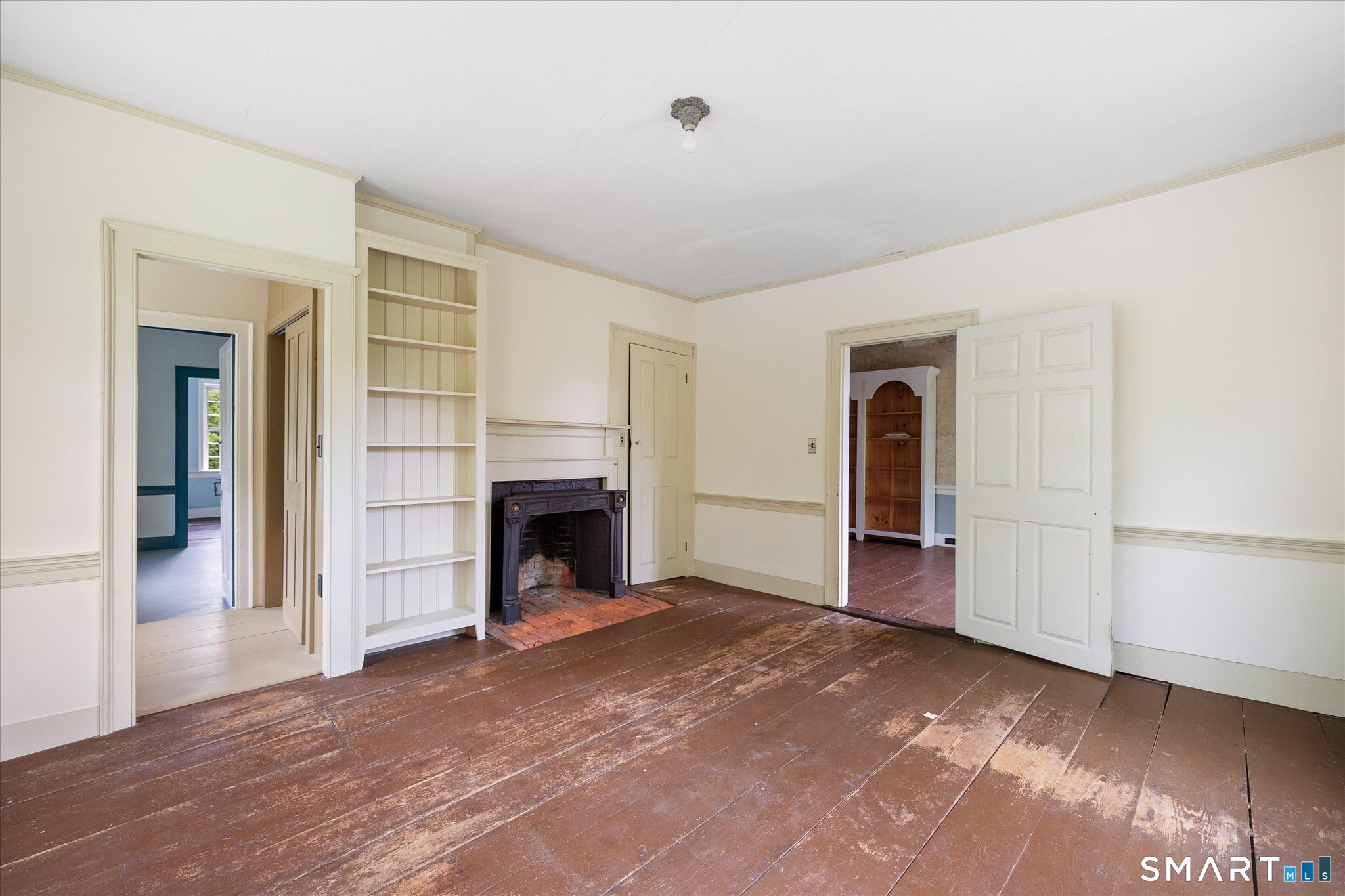 Empty room with a brick fireplace, built-in shelves, and worn wide-plank wood floors.
