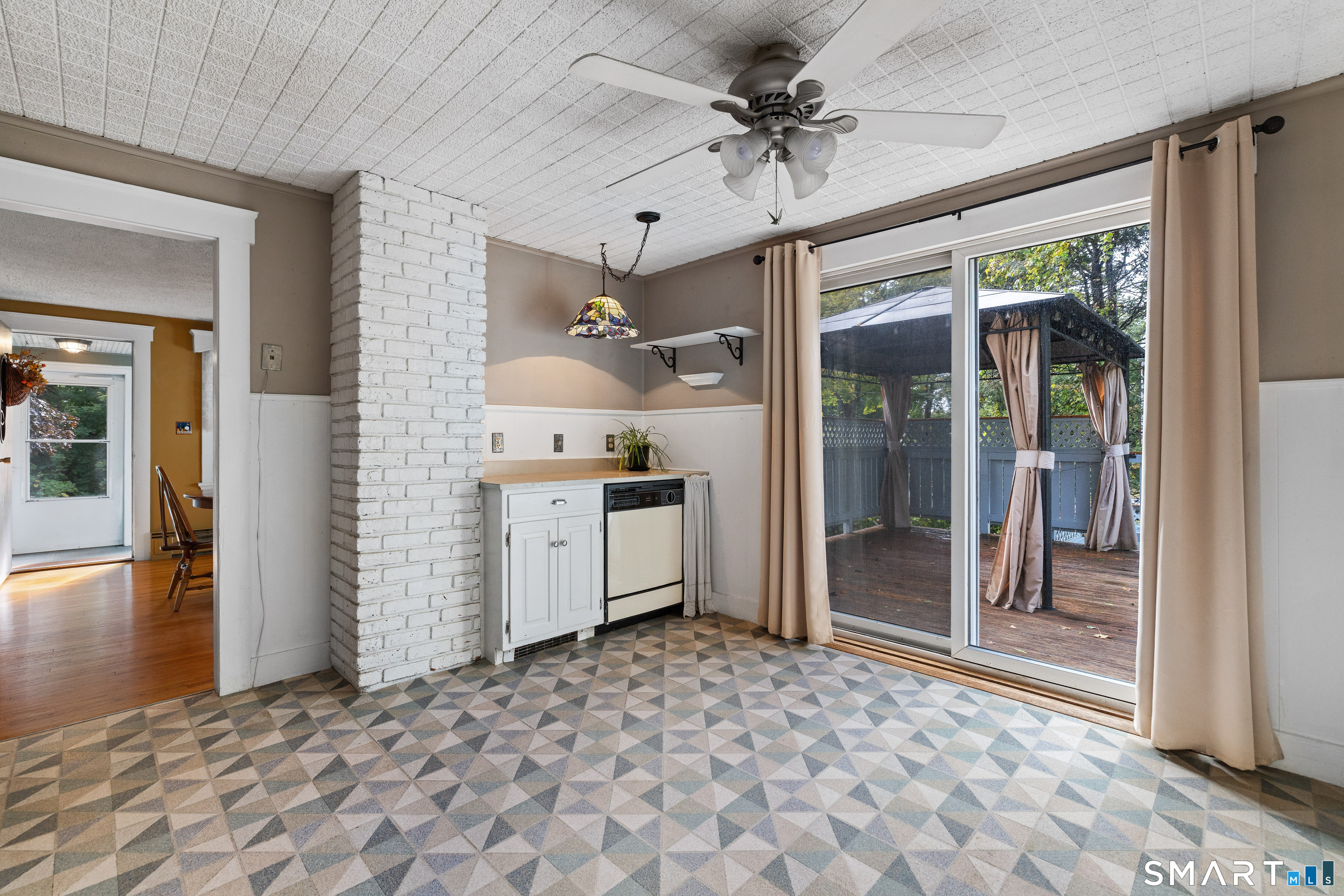 Tiled room with white brick column and sliding doors opening onto a deck with a curtained gazebo.