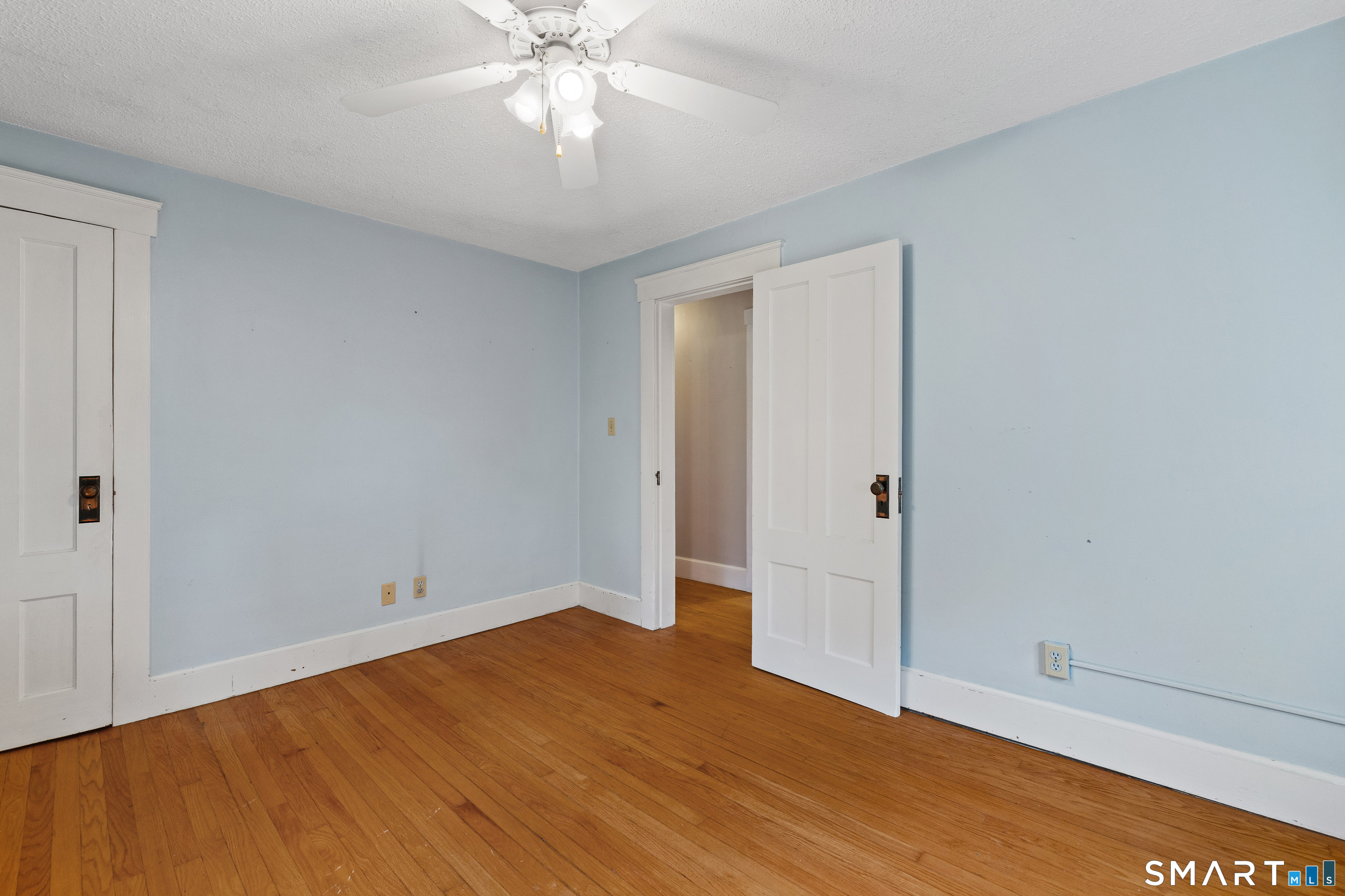 Empty blue-walled room with hardwood floors, a ceiling fan, and an open paneled door.