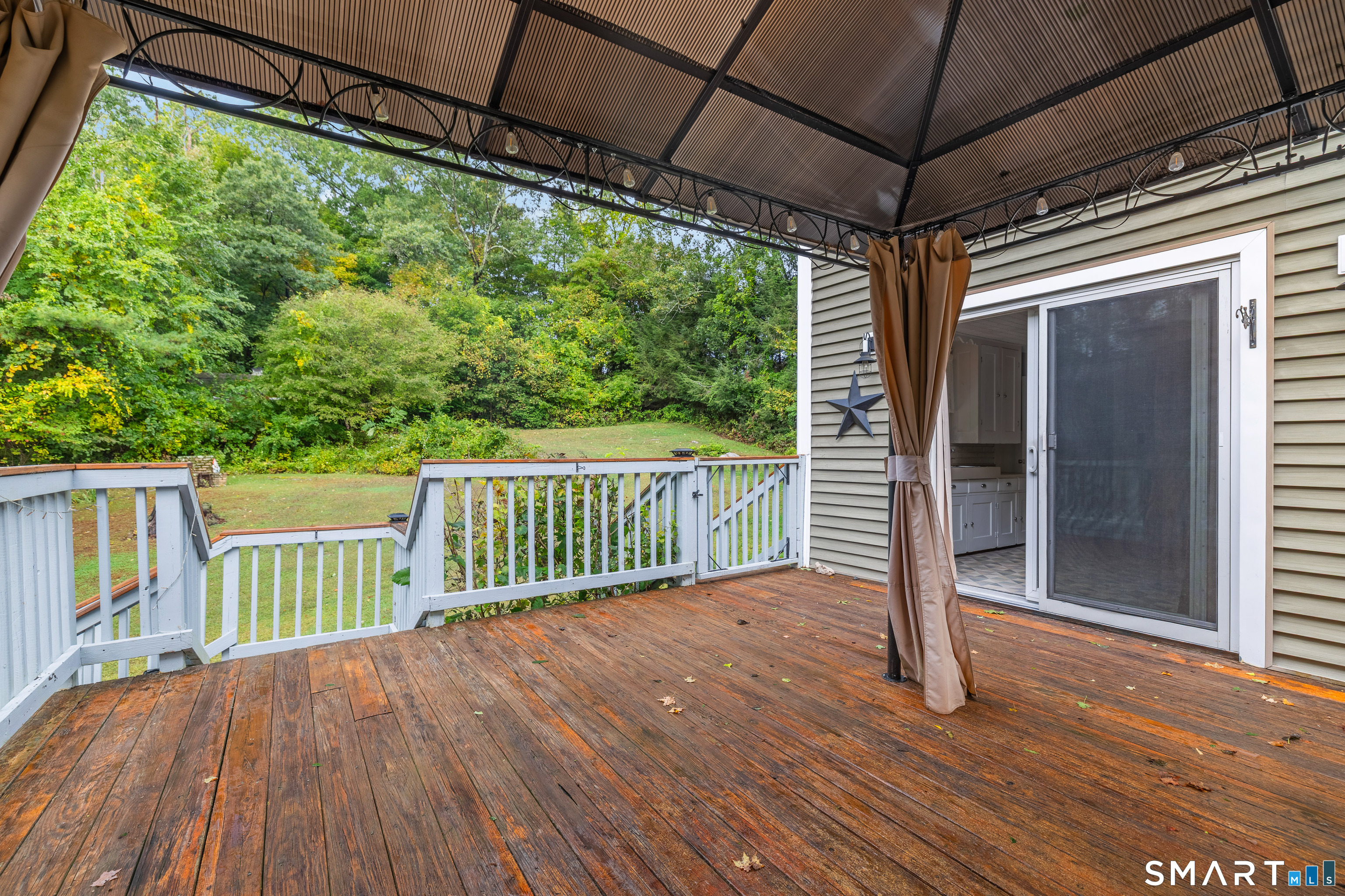 Covered wooden deck overlooking a leafy yard, with white railings and a sliding glass door.