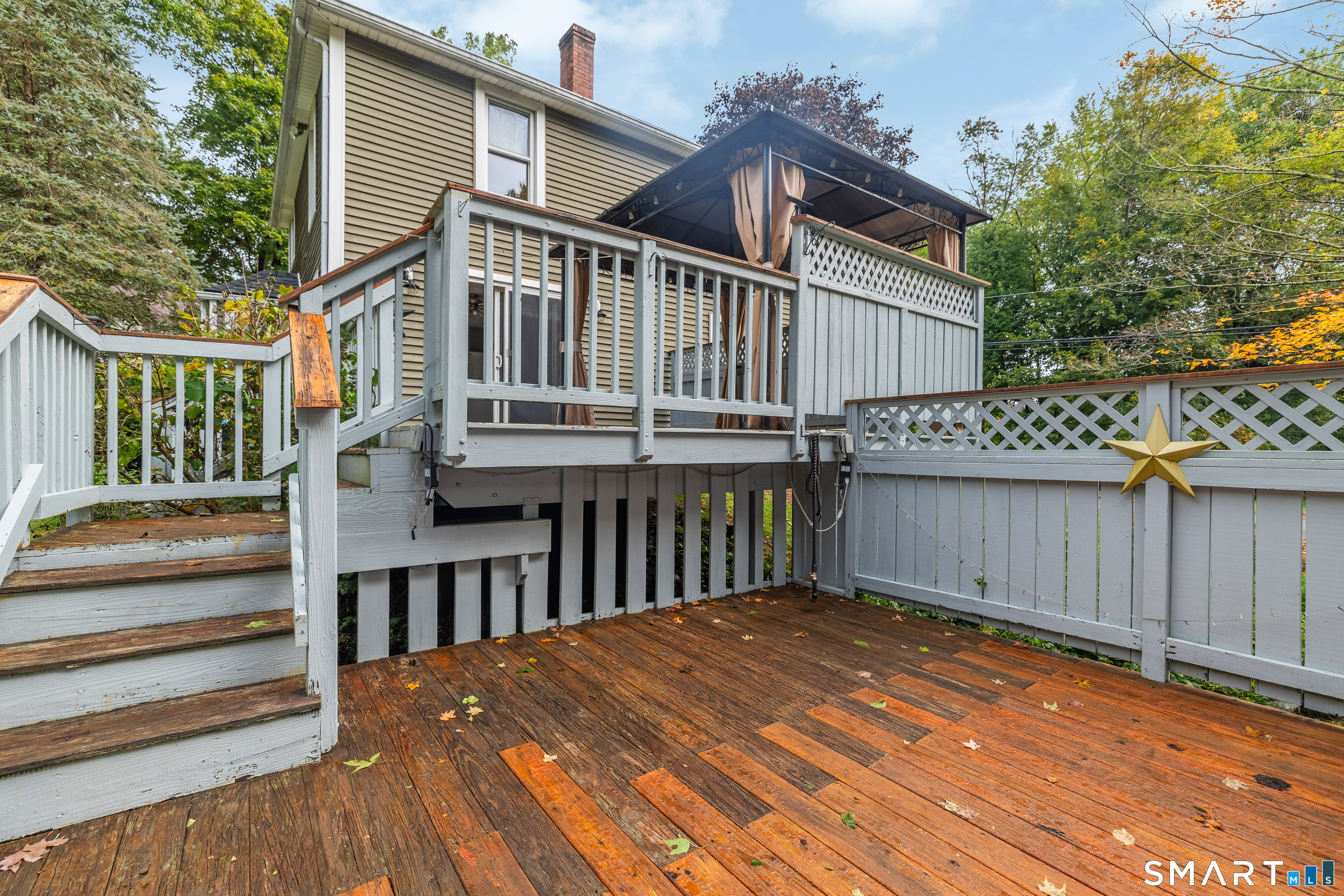 Wooden deck with gray railings and steps beside a two-story house, with an elevated covered deck above.