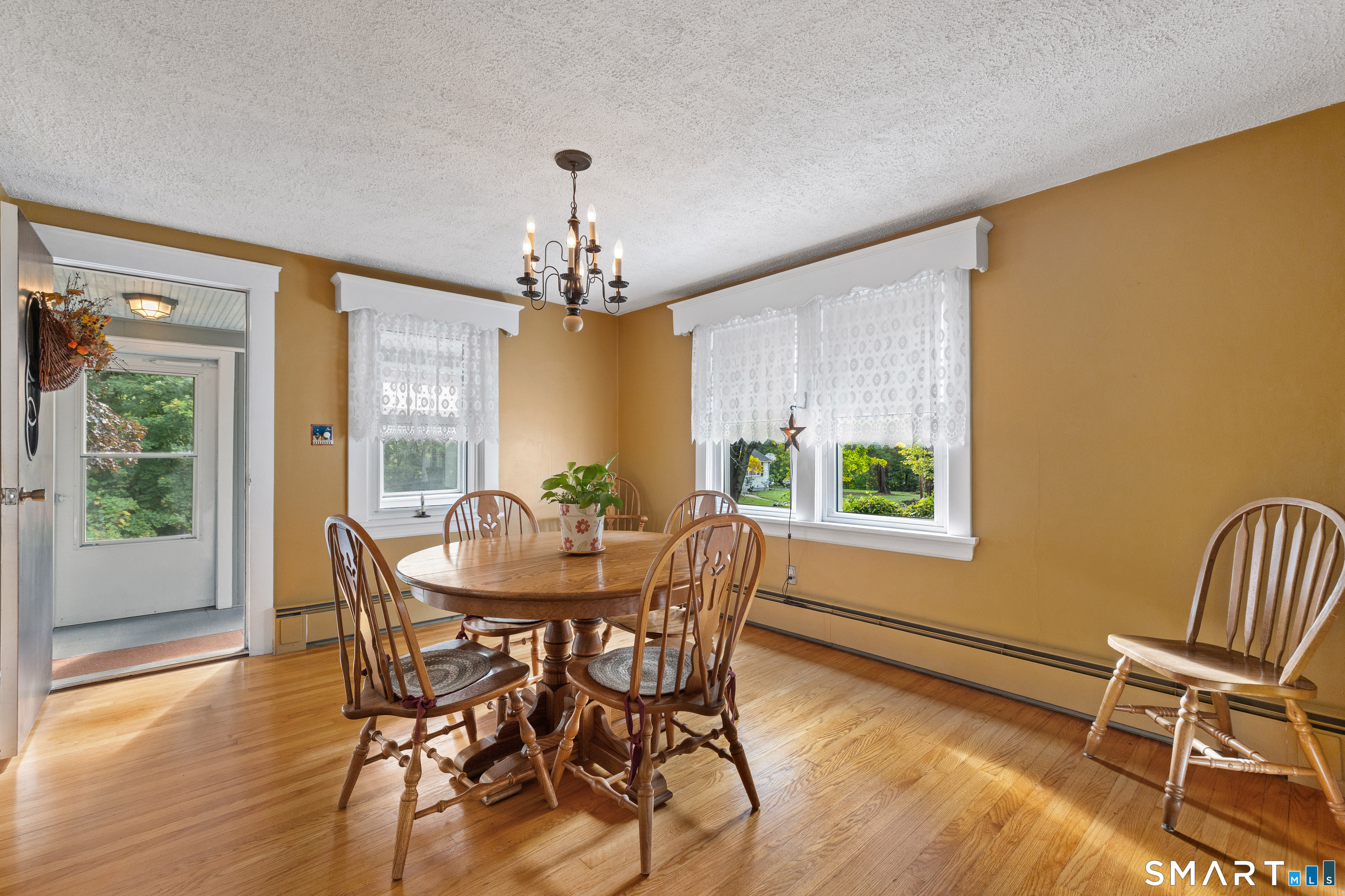 Dining room with a wooden table, hardwood floors, ochre walls, and lace-curtained windows.