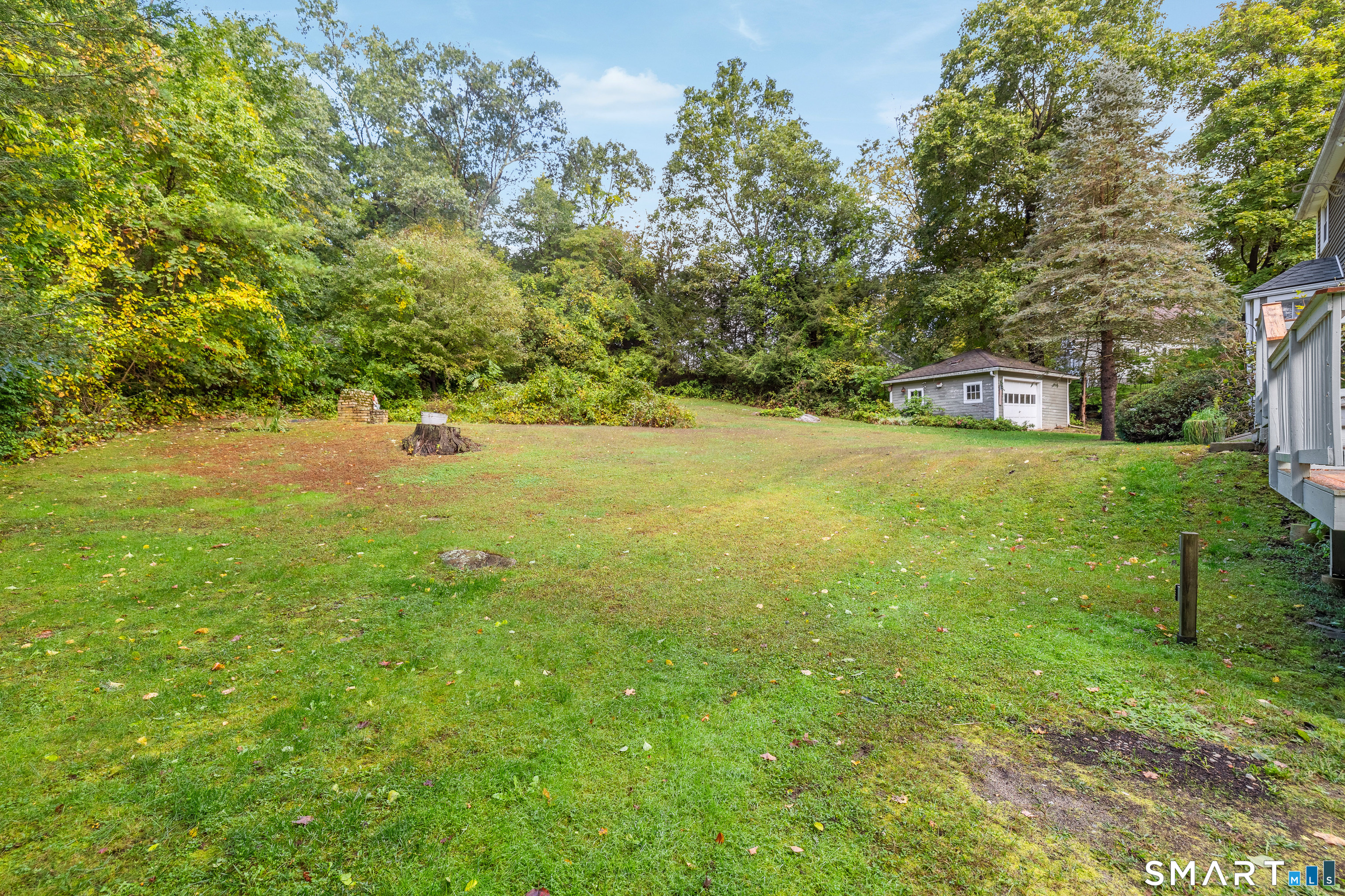 Grassy backyard bordered by mature trees, with a detached shed and part of the house visible.