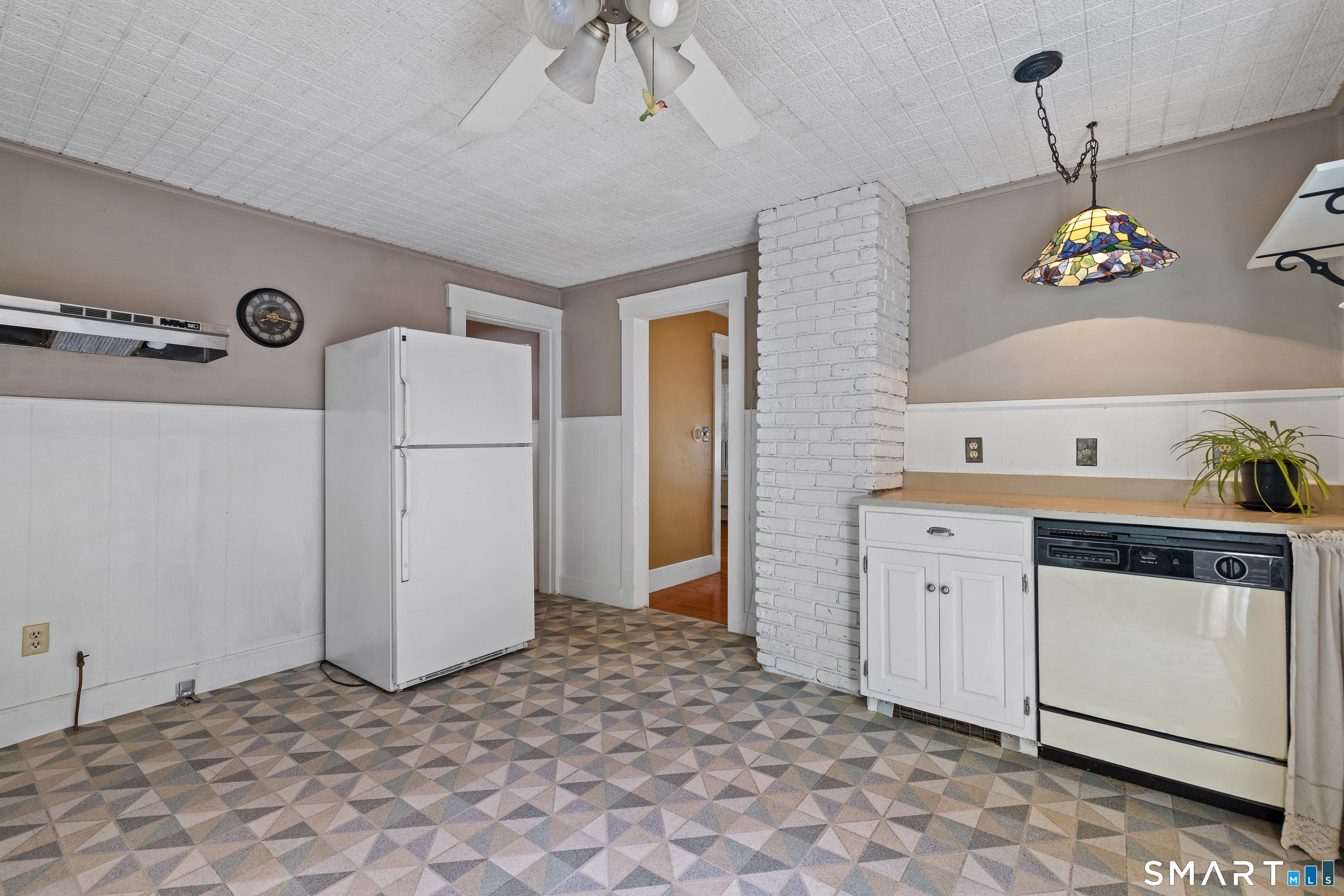 Kitchen with a white refrigerator, painted brick column, geometric-patterned floor, and stained-glass pendant light.