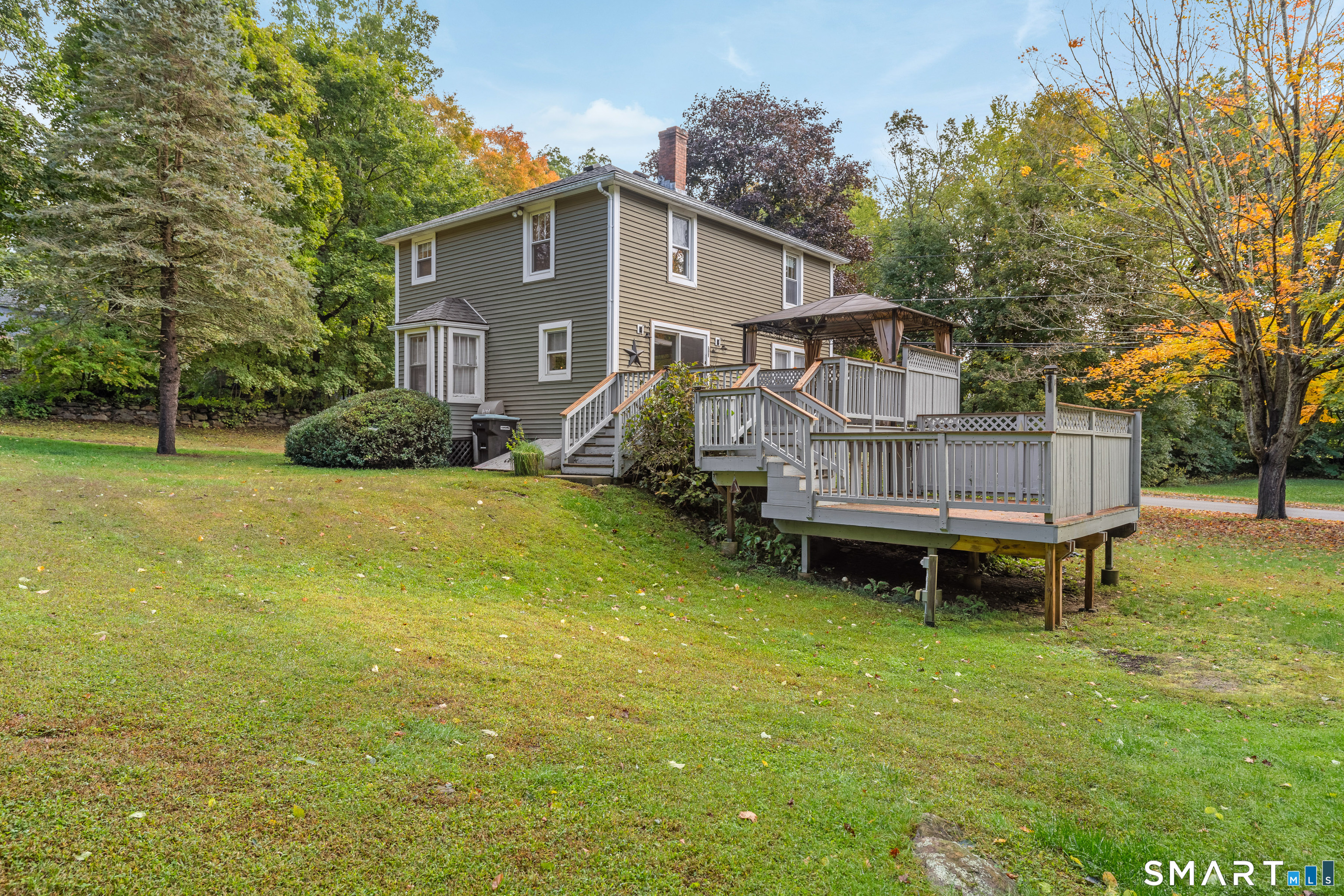 Two-story house with expansive raised decks and covered patio, surrounded by lawn and autumn trees.