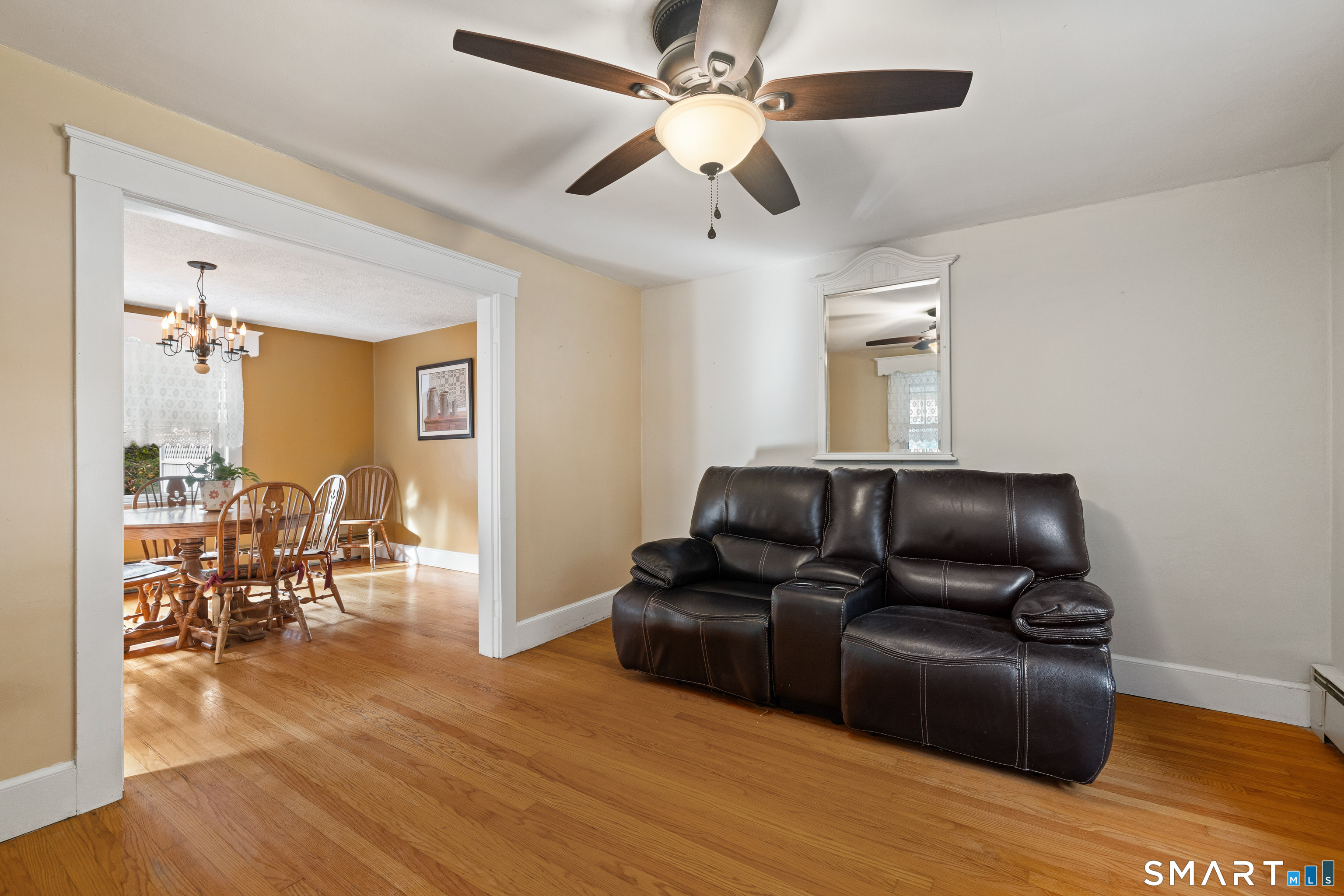 Living room with a dark leather reclining sofa and ceiling fan, opening onto a dining room with hardwood floors.
