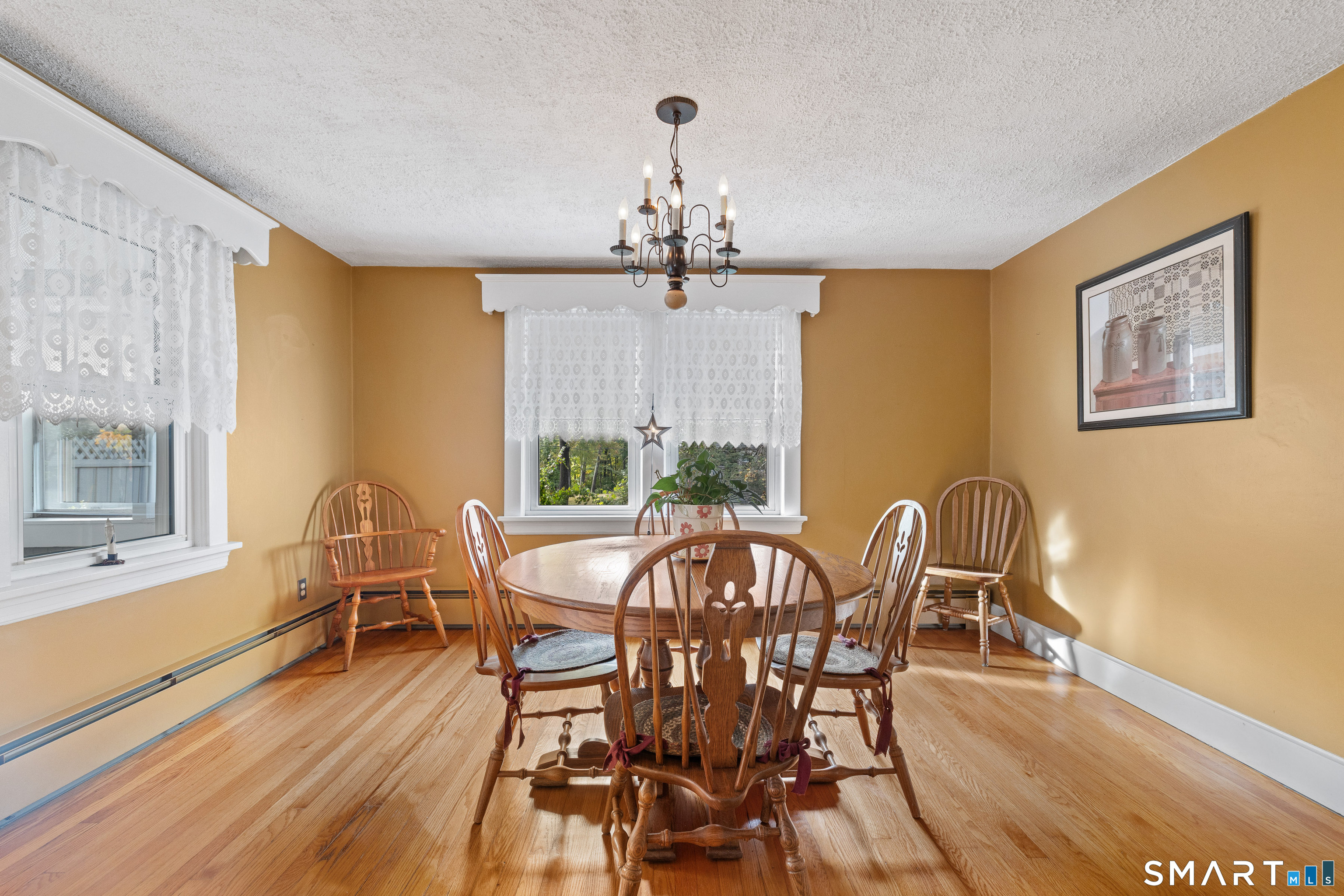 Dining room with a round wooden table, lace-curtained windows, and hardwood floors.