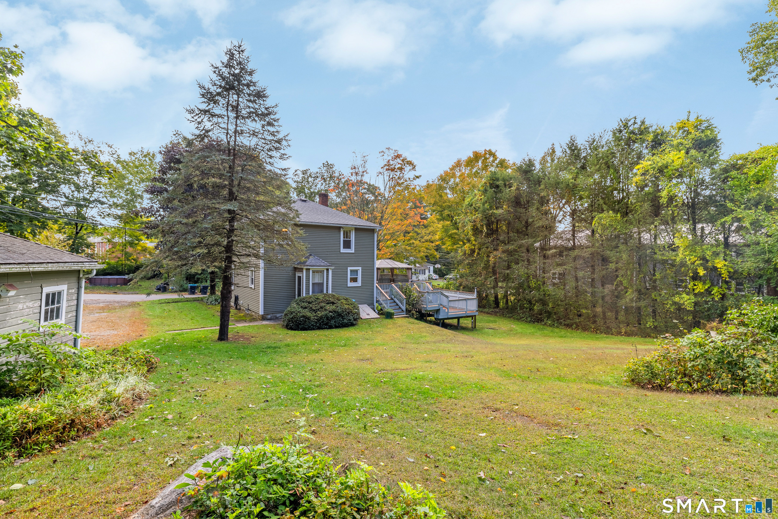 Two-story gray house with a raised deck overlooking a broad lawn and autumn trees.