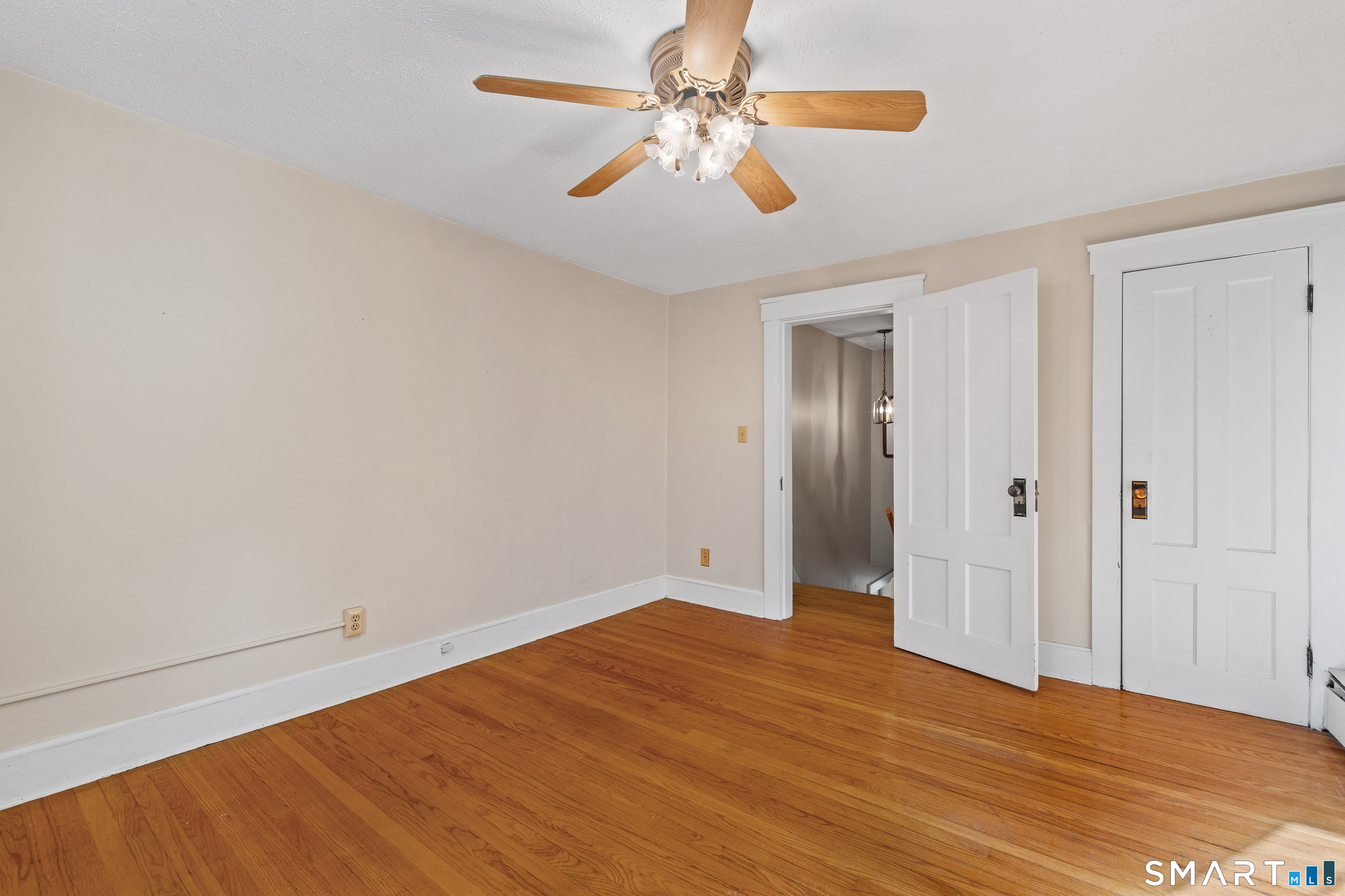 Vacant room with hardwood floors, a wood-blade ceiling fan, and two white doors.