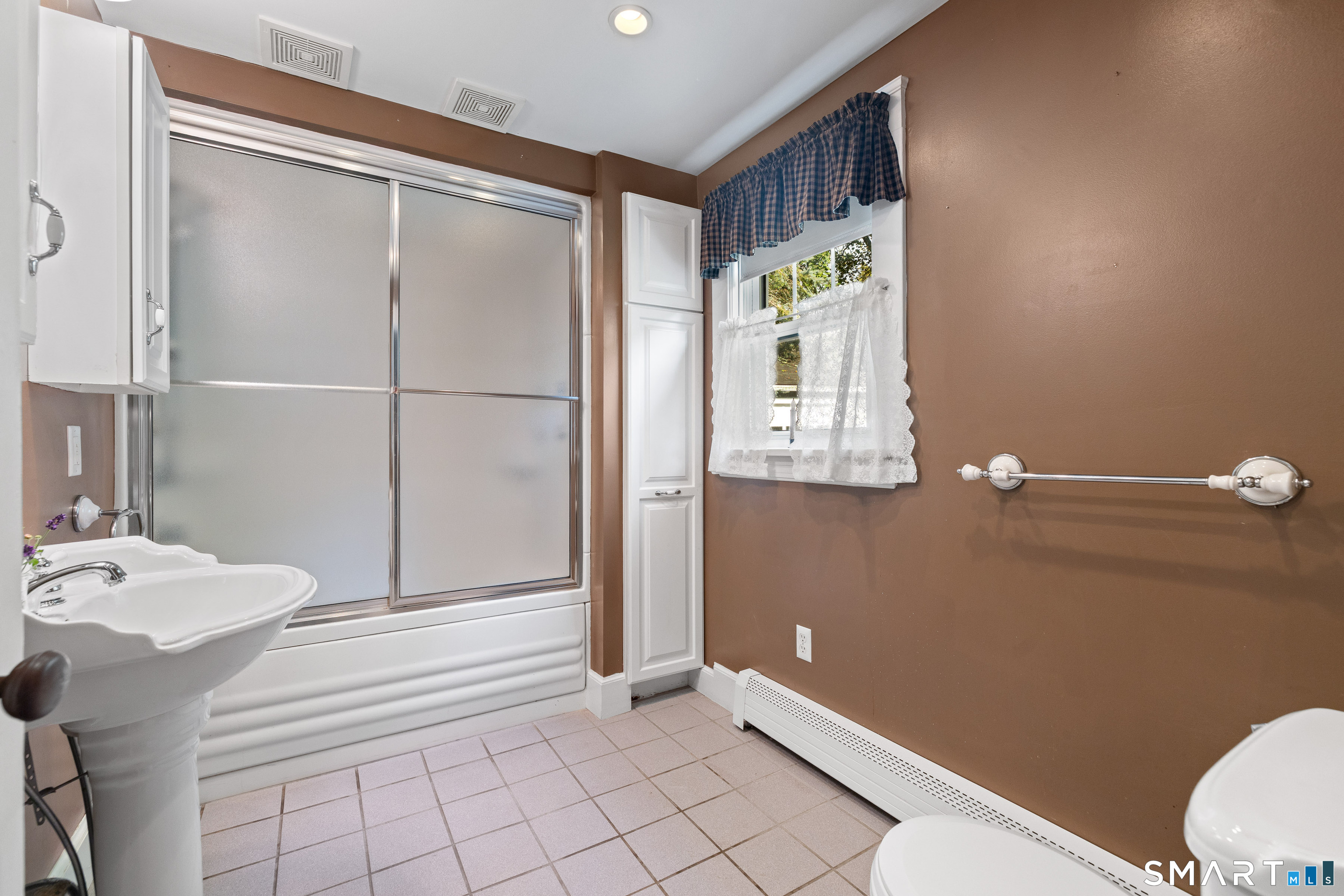 Bathroom with a pedestal sink, tiled floor, and tub behind frosted sliding shower doors.