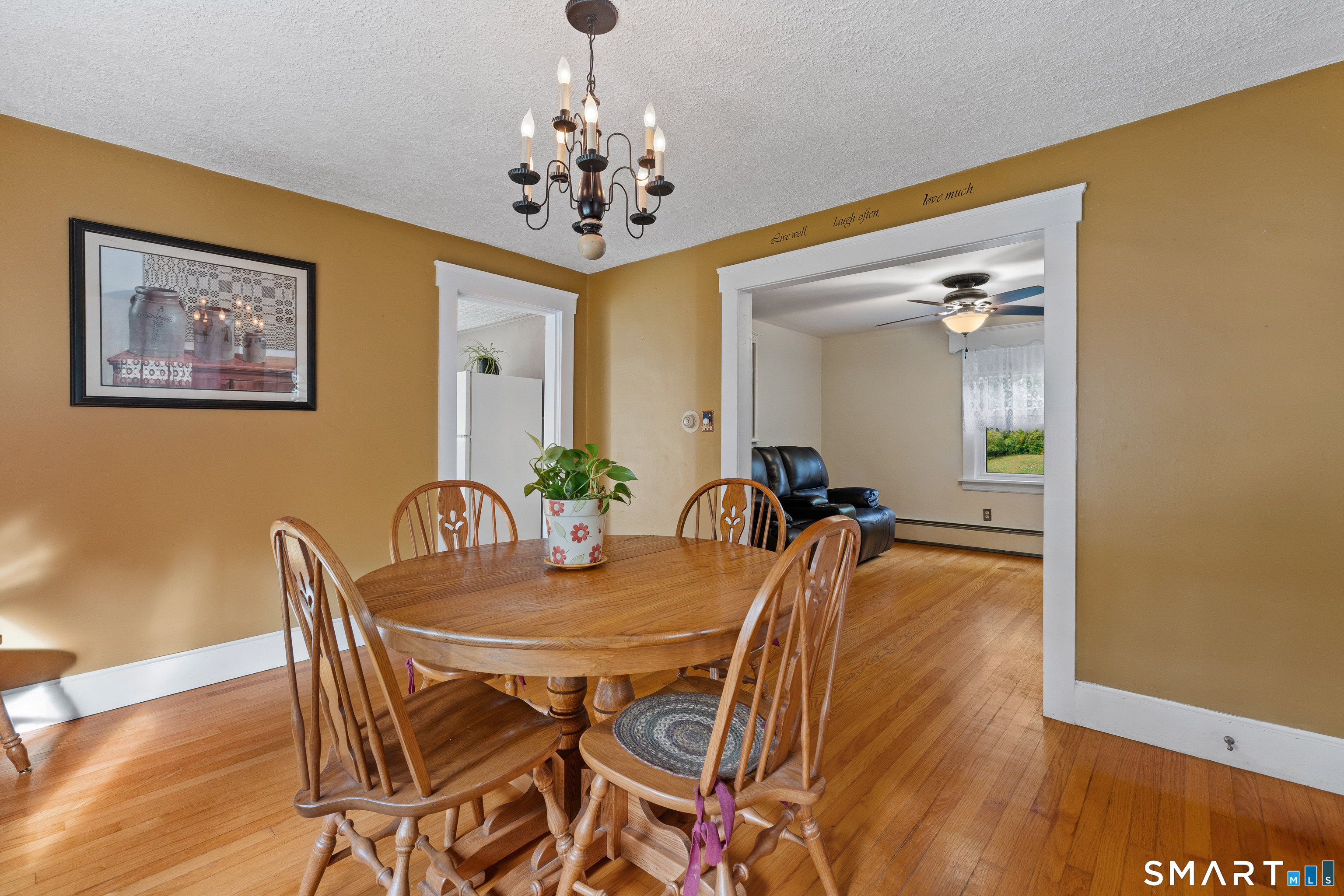 Dining room with a wooden table and chandelier, opening into a living room with a black recliner.