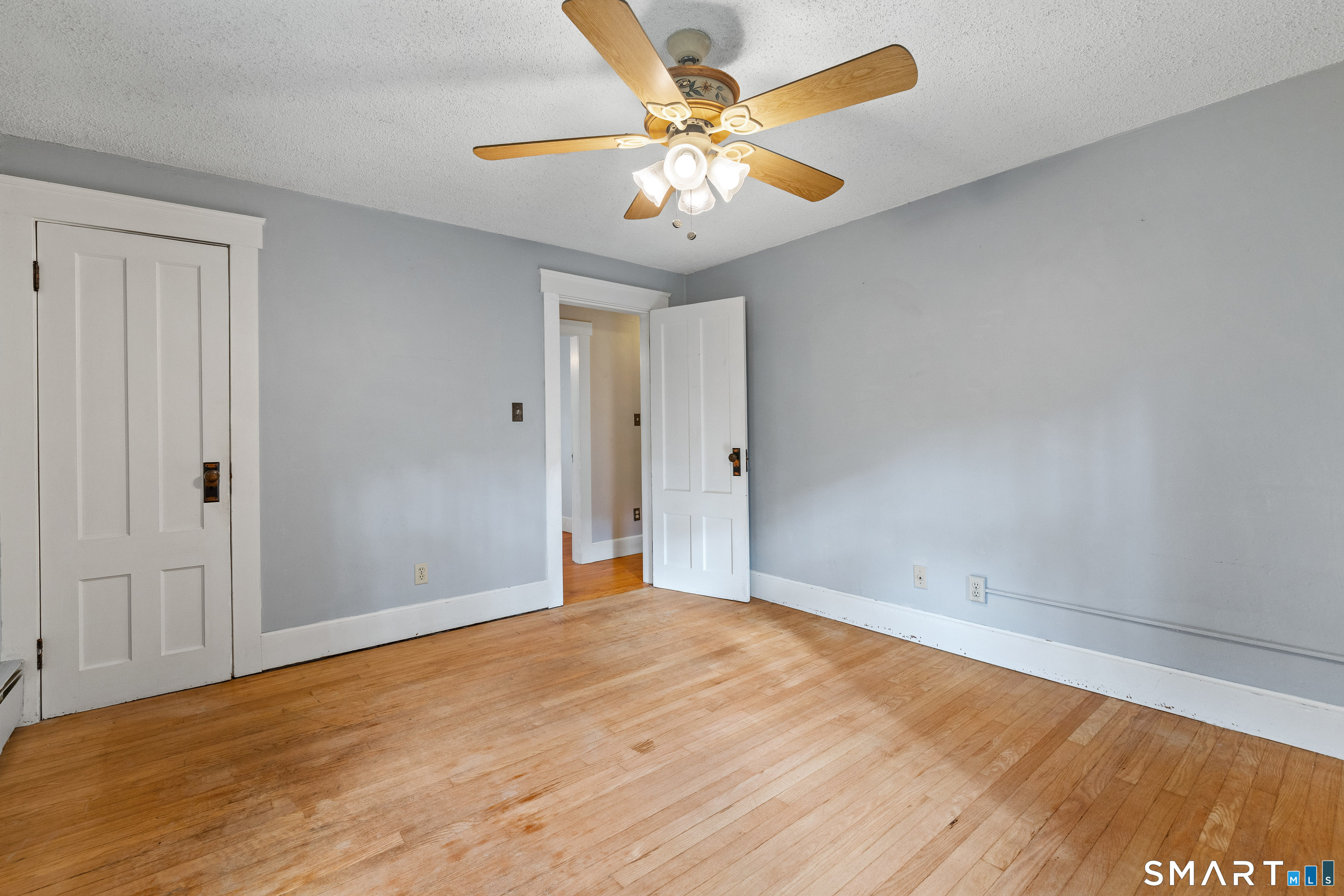 Empty room with hardwood floors, gray walls, white paneled doors, and a ceiling fan.