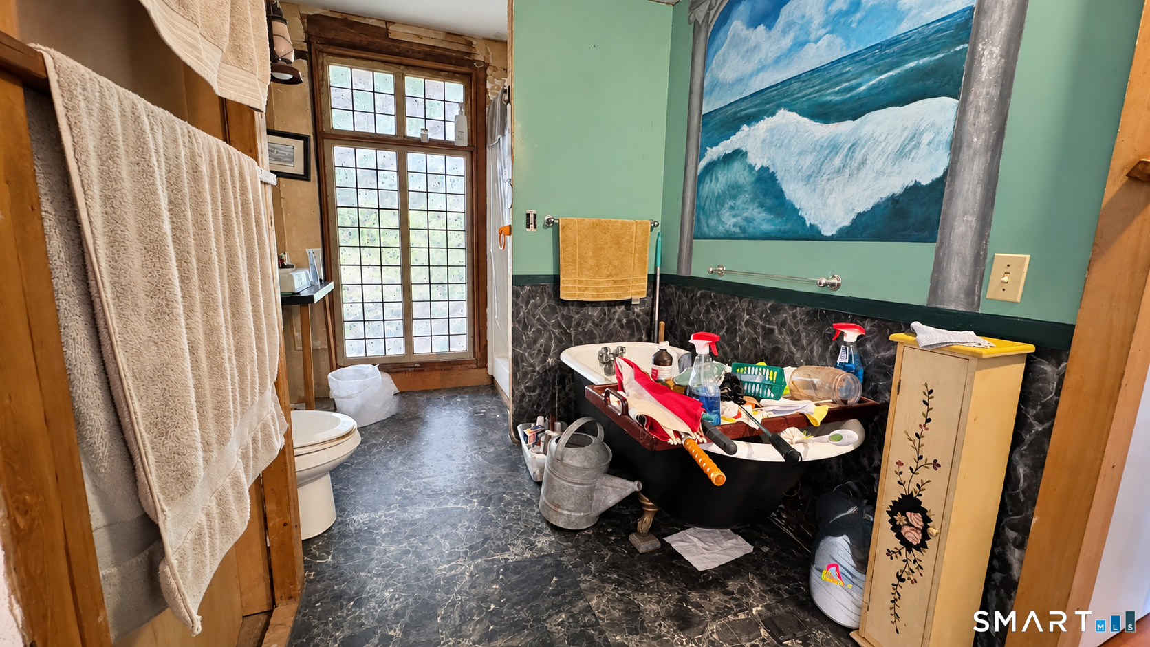 Bathroom with a black clawfoot tub, green walls, and a large ocean-wave painting.