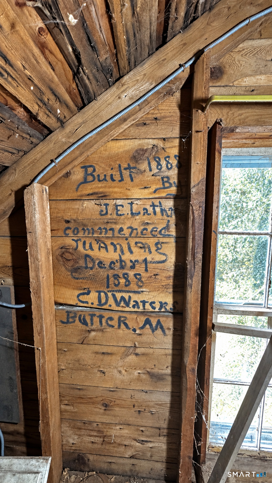 Exposed timber framing with handwritten 1888 construction notes beside a tall window.