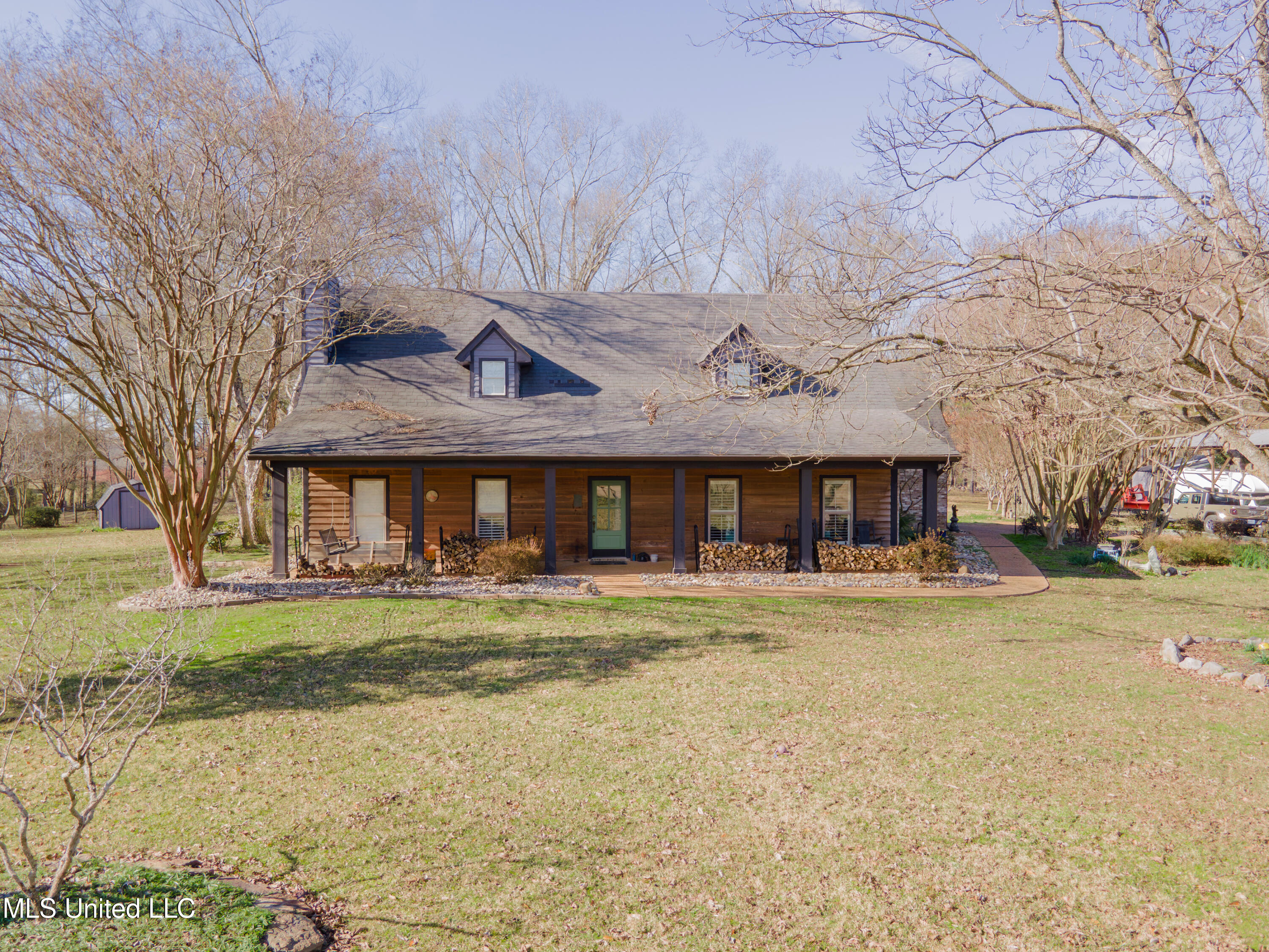 Wood-sided home with a covered porch, green front door, and leafless trees across the lawn.
