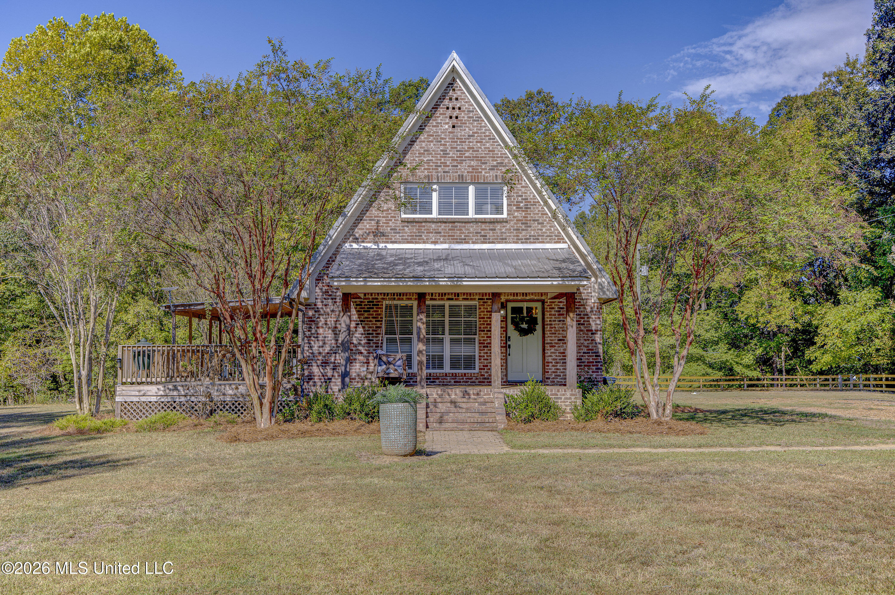 Brick A-frame house with a covered porch and side deck, framed by mature trees.