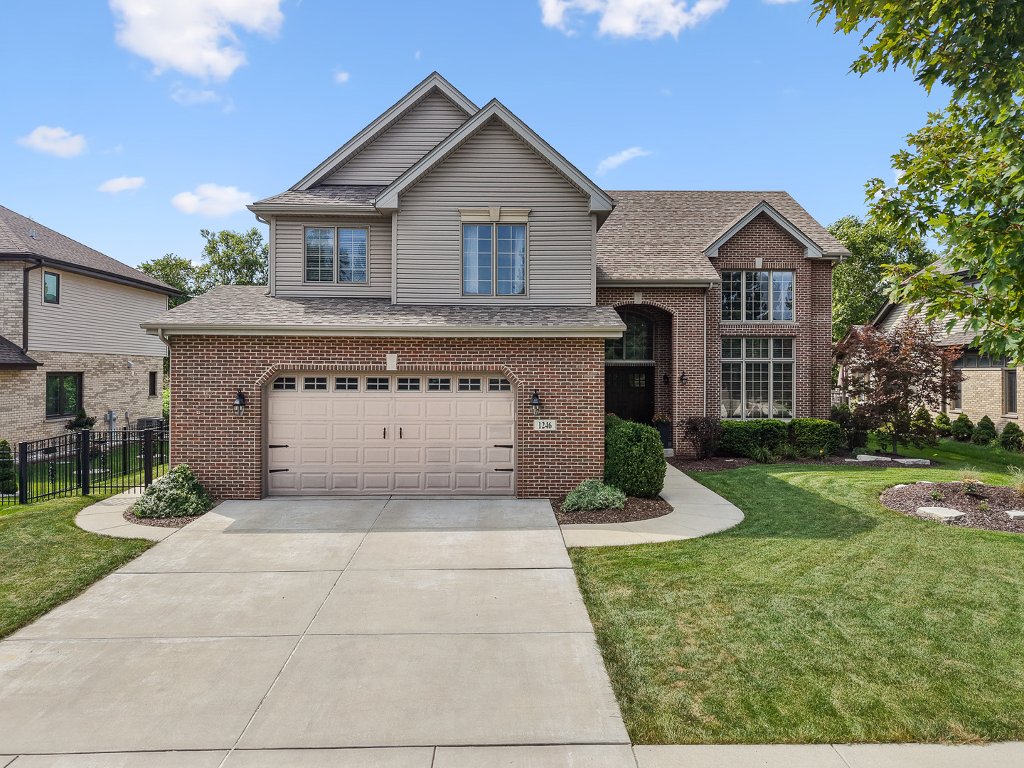 Two-story brick and taupe-sided house with a double garage, broad driveway, and landscaped front lawn.