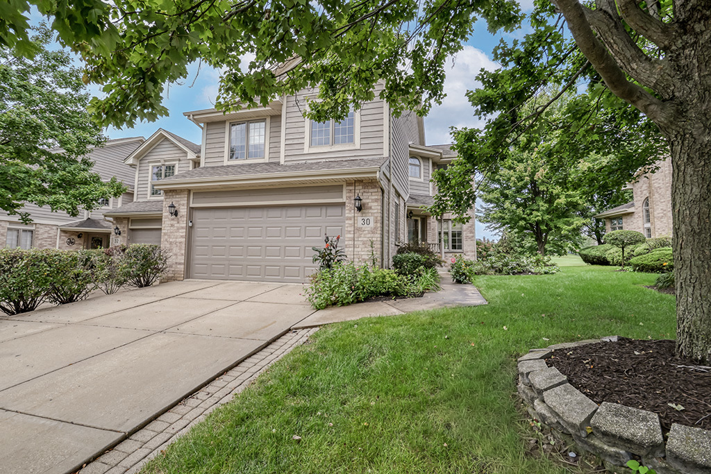 Two-story attached home with a double garage, stone accents, and a tree-shaded lawn.