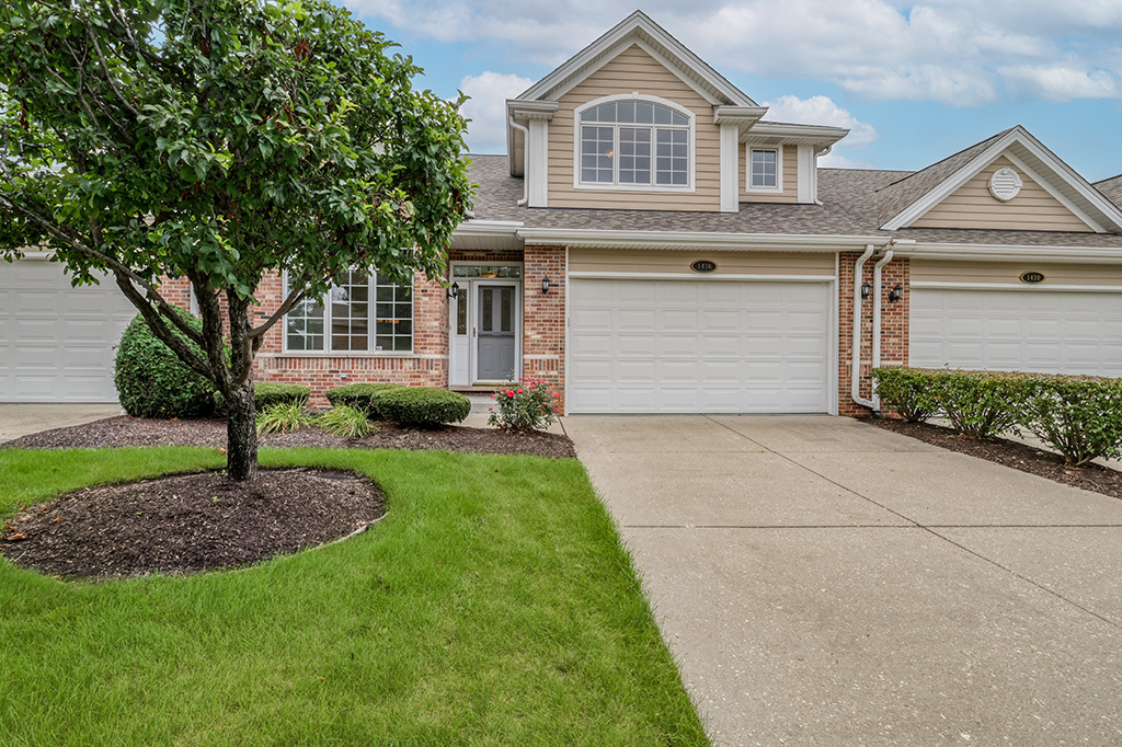 Two-story brick-and-beige home with a double garage, wide driveway, and mature tree in the front lawn.