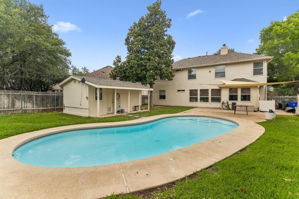 Back of a two-story home with a curved swimming pool, patio, and detached poolside structure.