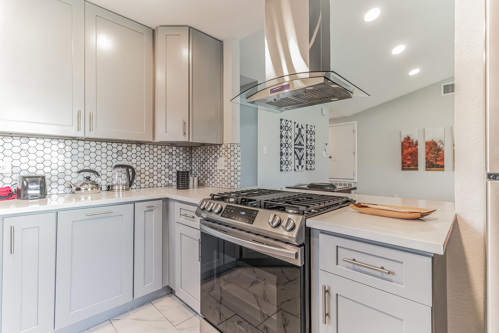 Modern kitchen with white cabinets, hexagonal tile backsplash, and a stainless steel range beneath a glass hood.