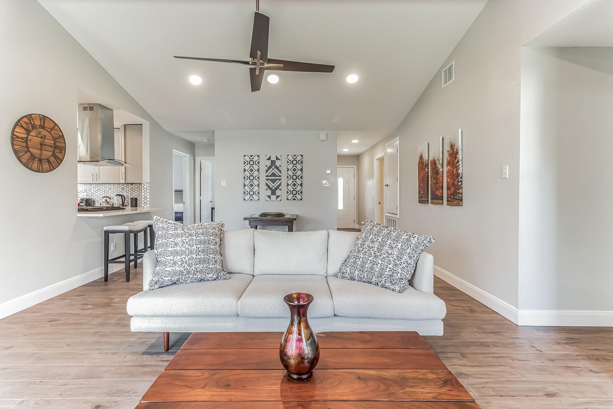 Living room with a white sofa and wood coffee table, opening onto a kitchen.