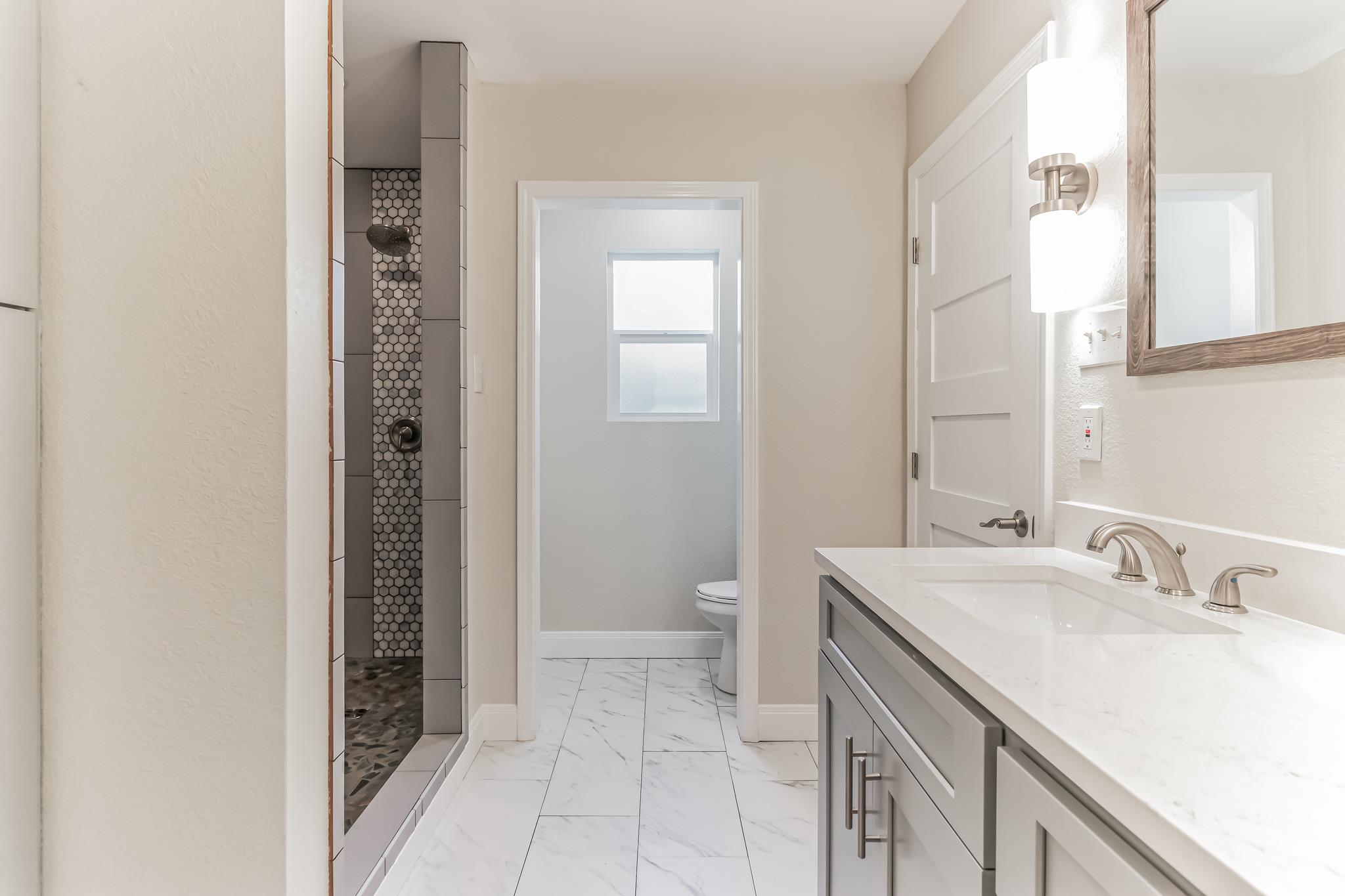 Bathroom with a gray vanity, marble-look tile floor, and walk-in shower with hexagonal mosaic tile.