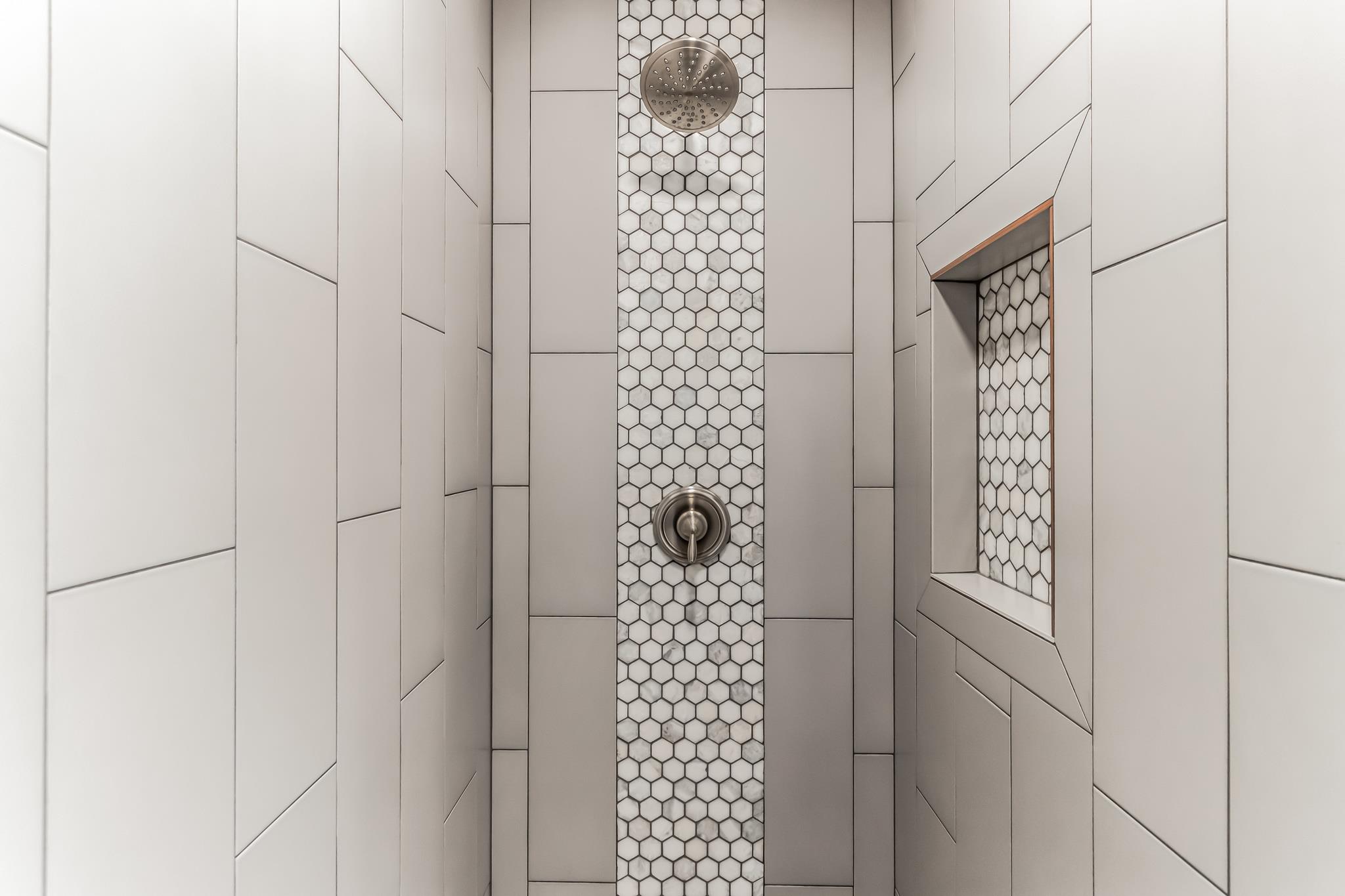 Walk-in shower with a honeycomb mosaic accent strip, rain showerhead, and recessed tiled niche.