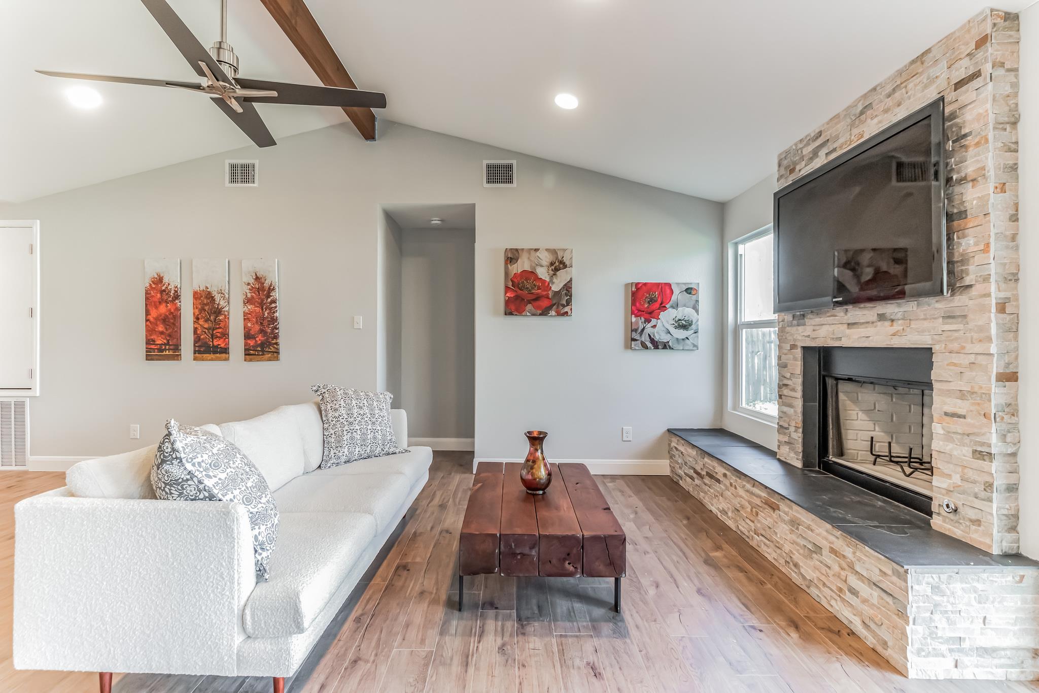 Living room with a vaulted ceiling, white sofa, and stone fireplace with mounted television.